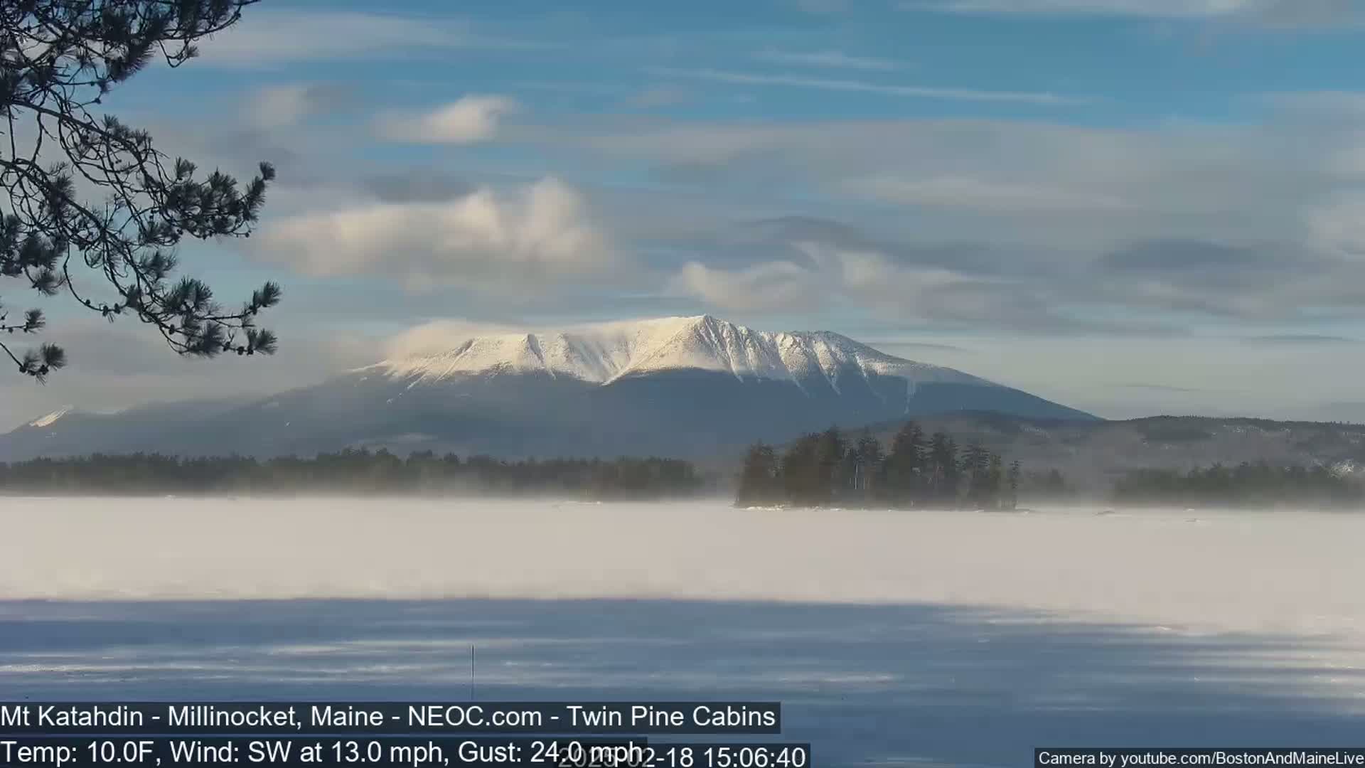 A snow-covered mountain range is visible across a foggy, frozen lake under a partly cloudy sky.