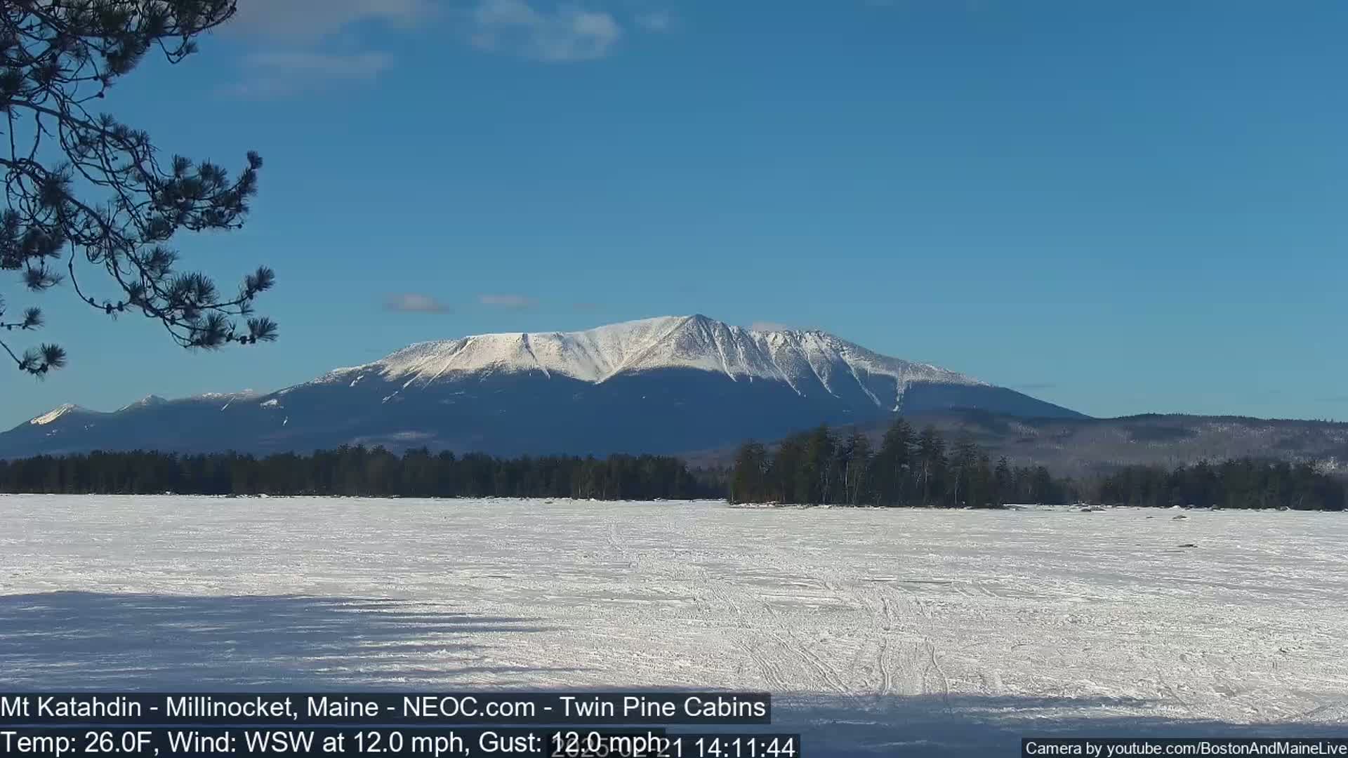 A snow-covered mountain range is visible in the distance across a frozen lake under a clear blue sky with a light wind.