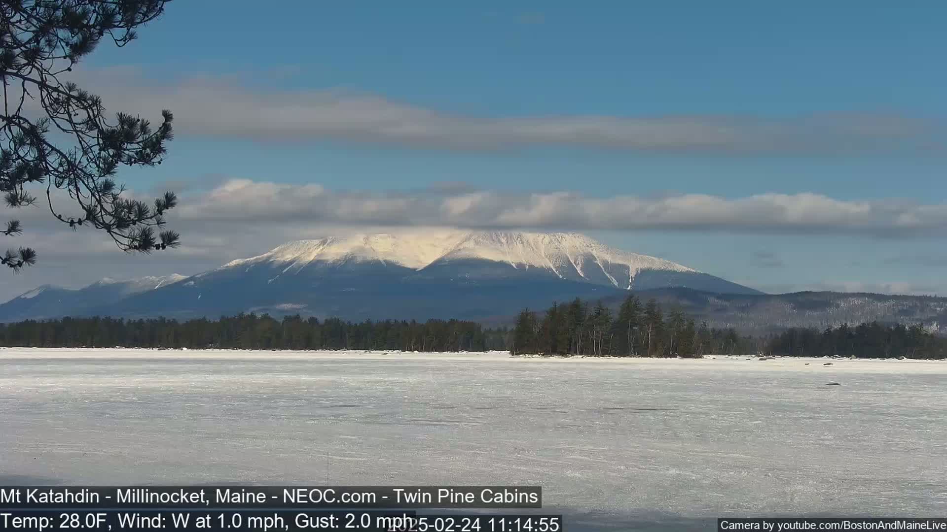 A snow-capped mountain is visible in the distance across a frozen lake under a partly cloudy sky.