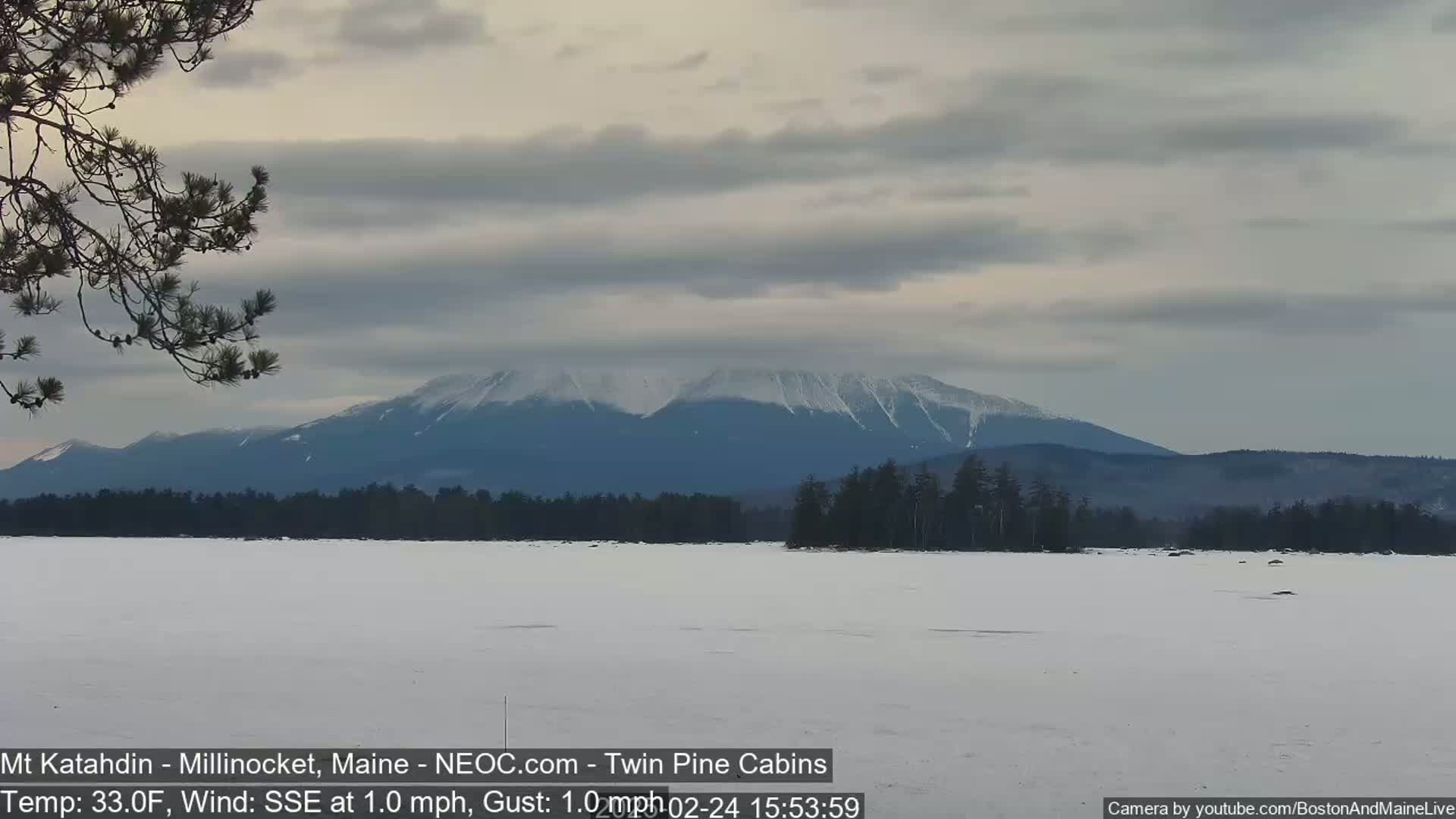 A snow-covered lake stretches to a distant, snow-capped mountain range under a cloudy sky.