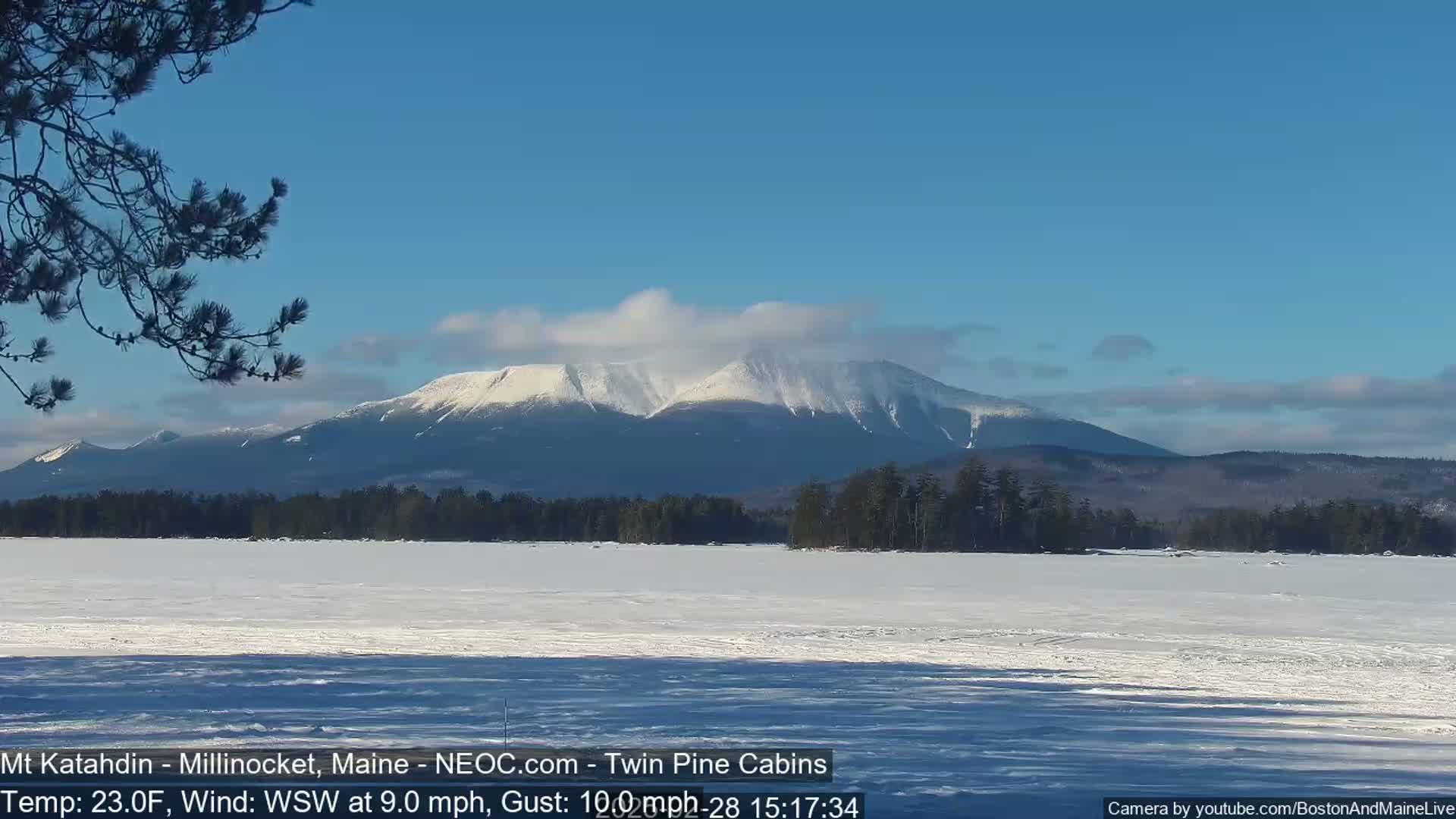 A snow-covered mountain range is visible in the distance across a frozen lake under a mostly clear blue sky.