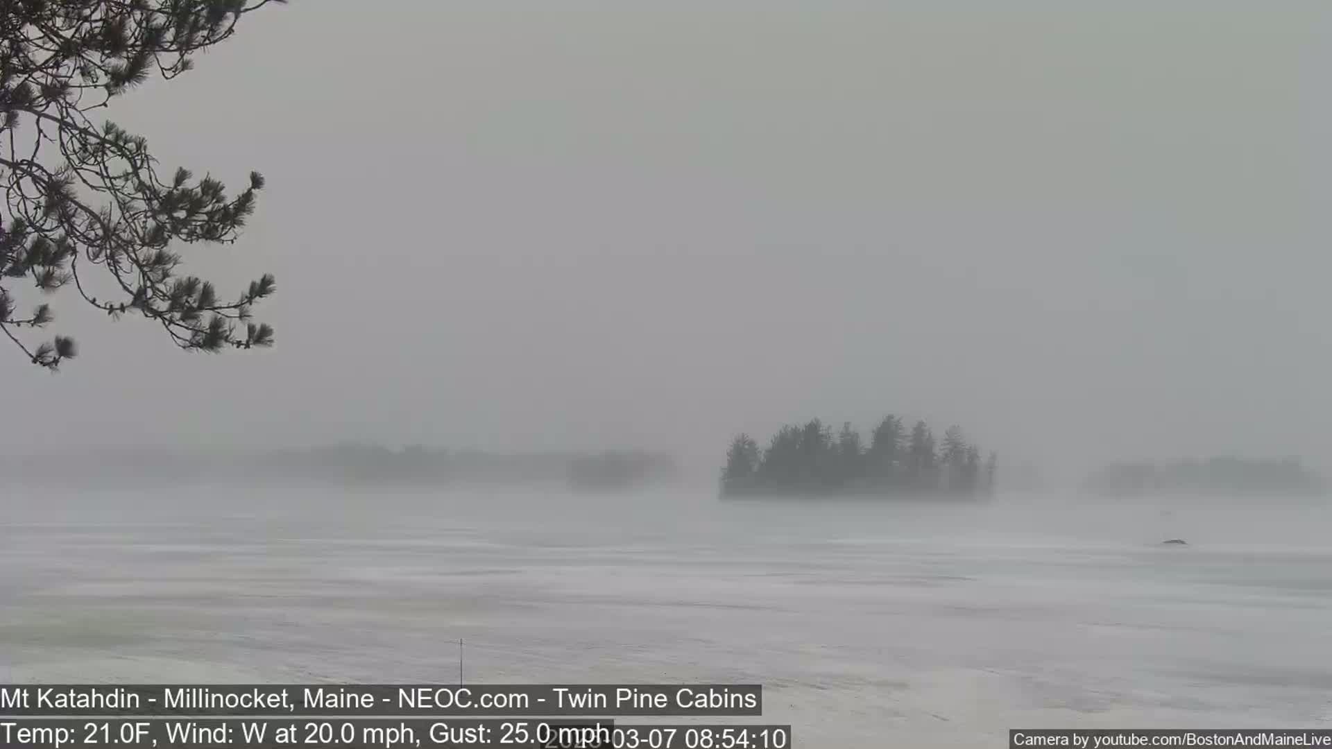A snow-covered, flat landscape with a few distant, indistinct islands is visible through a heavy, blowing snowstorm.