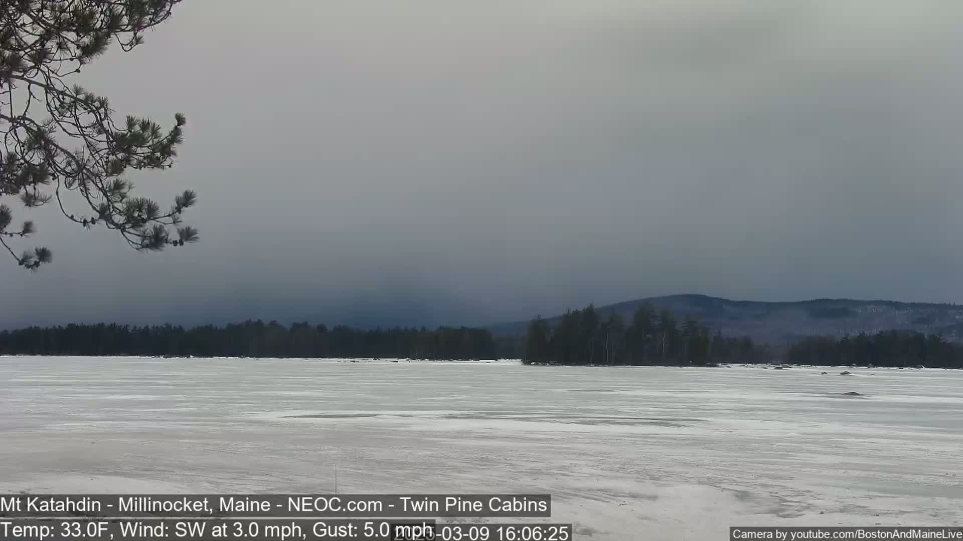 A partially frozen lake stretches toward a distant, hazy mountain range under an overcast sky.