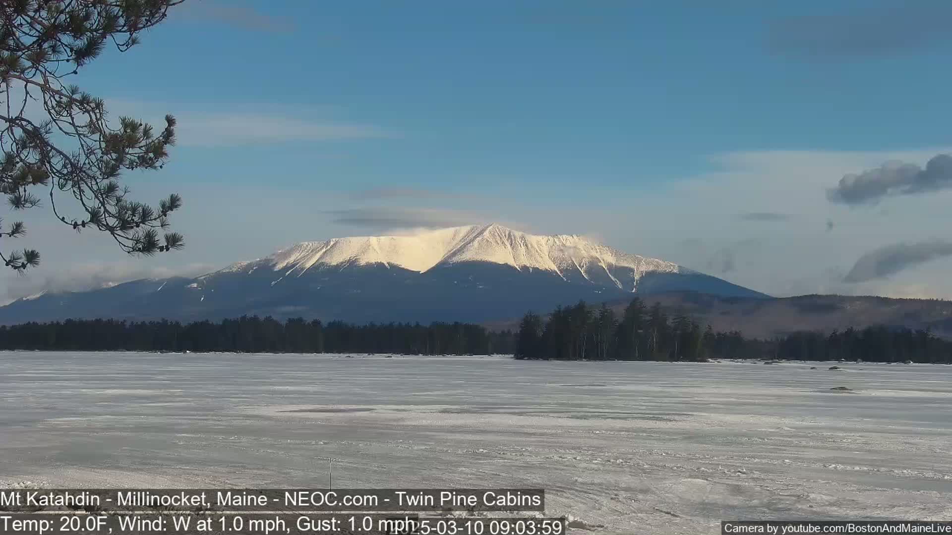 A snow-capped mountain is visible in the distance across a frozen lake under a mostly clear blue sky.