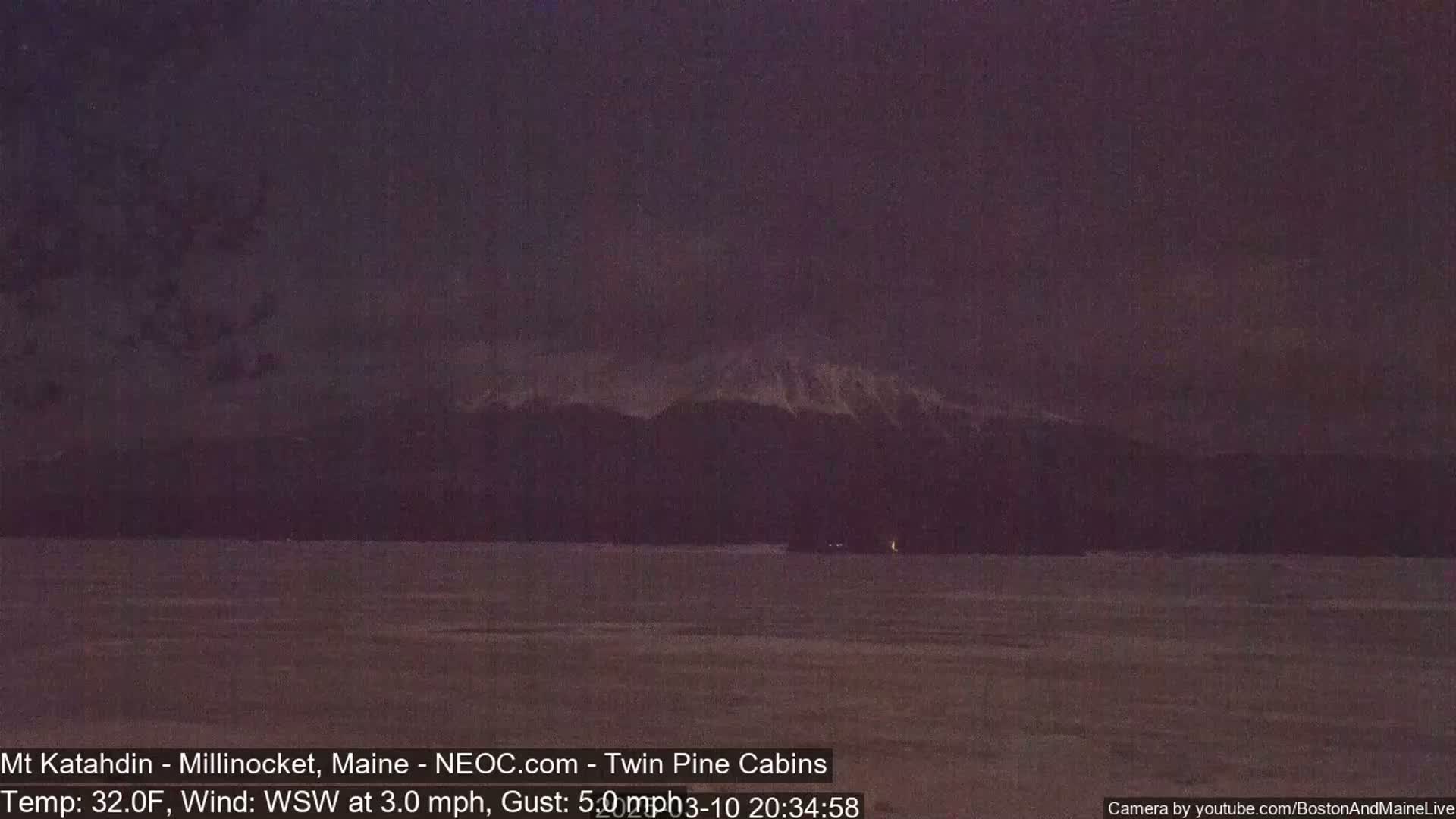 A dark, snow-dusted mountain range is visible in the distance across a flat, dark expanse under a dusky sky with a light wind.