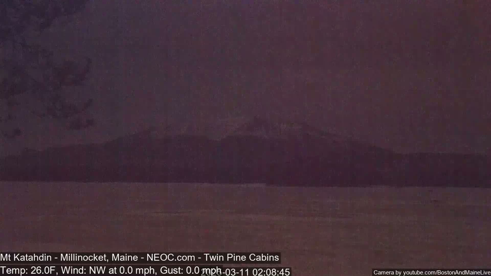 A dark, still body of water stretches toward snow-capped mountains under a dusky sky.
