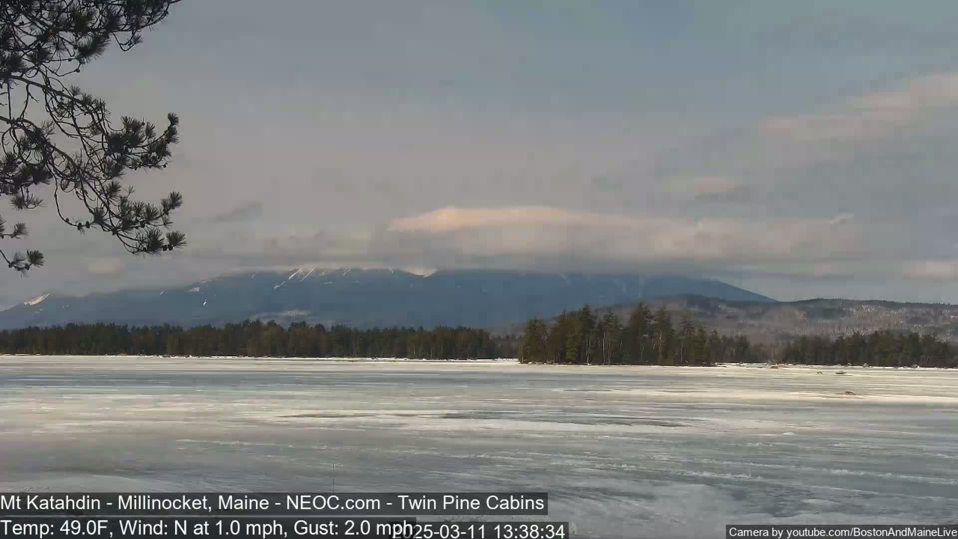 A partially frozen lake stretches out before a mountain range under a mostly cloudy sky.