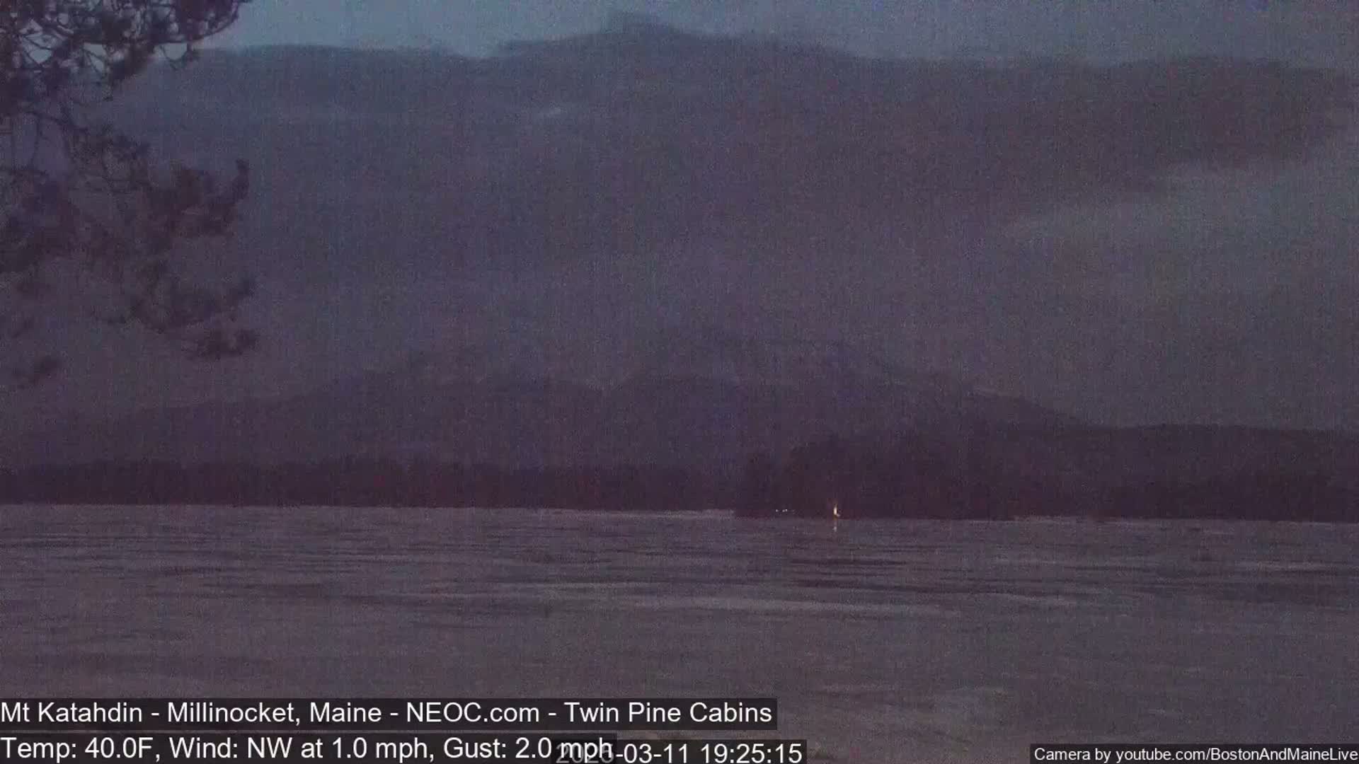 A dark, overcast sky hangs over a frozen lake with distant mountains visible in the background, under a cool, 40°F temperature with a light northwest wind.
