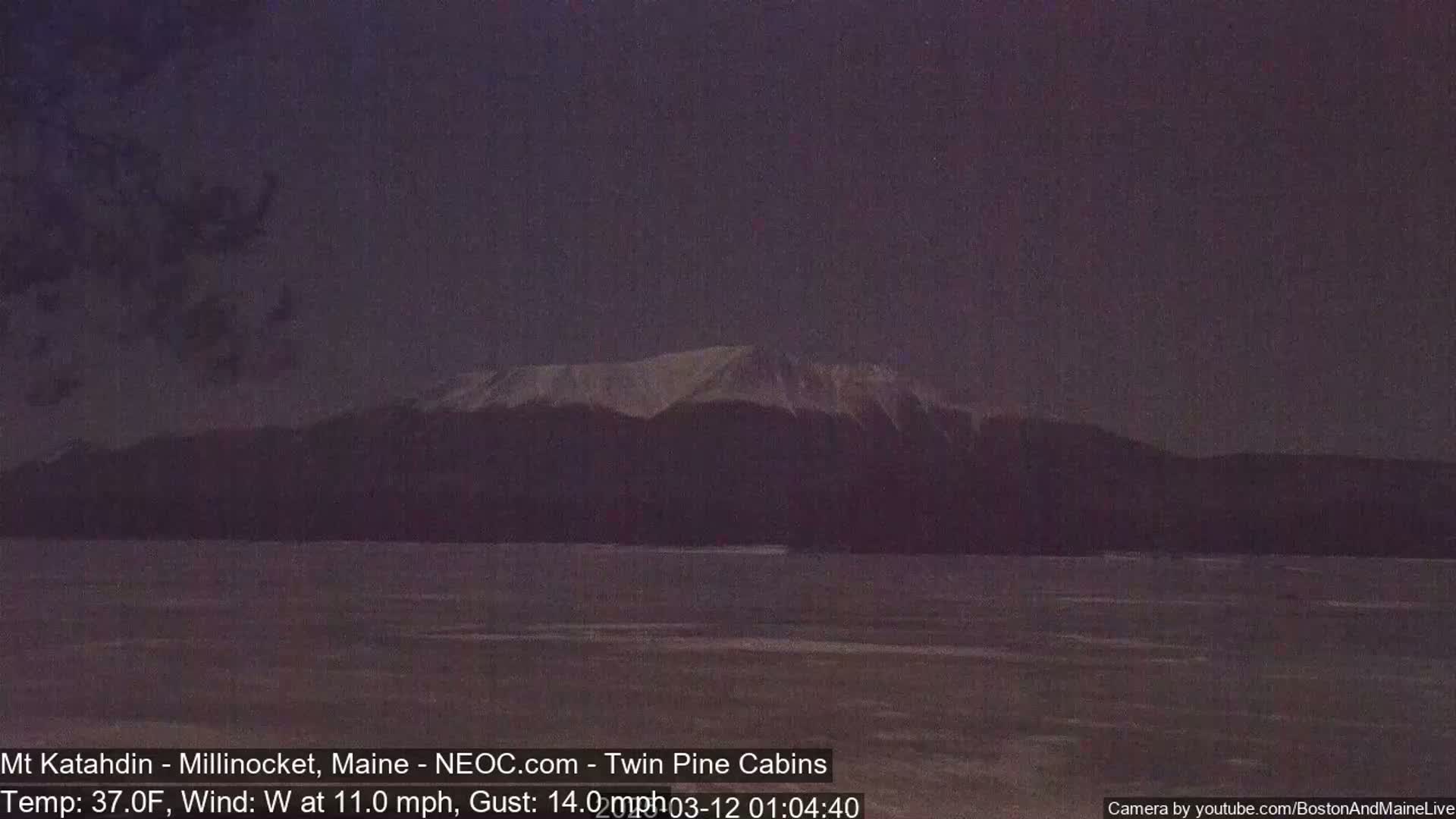 A snow-capped mountain range is visible across a dark, still body of water under a twilight sky.
