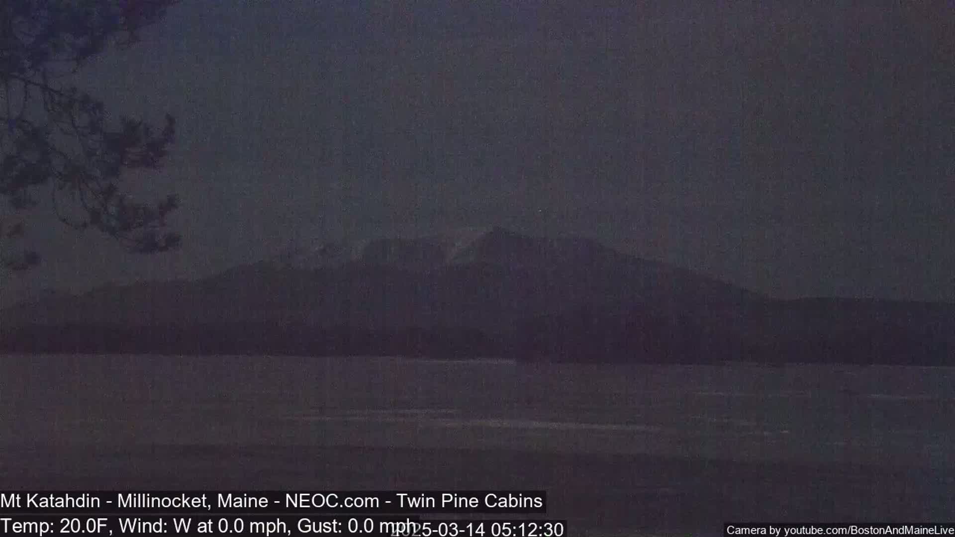 A dark, calm body of water sits in front of a silhouetted mountain range under a dusky sky.