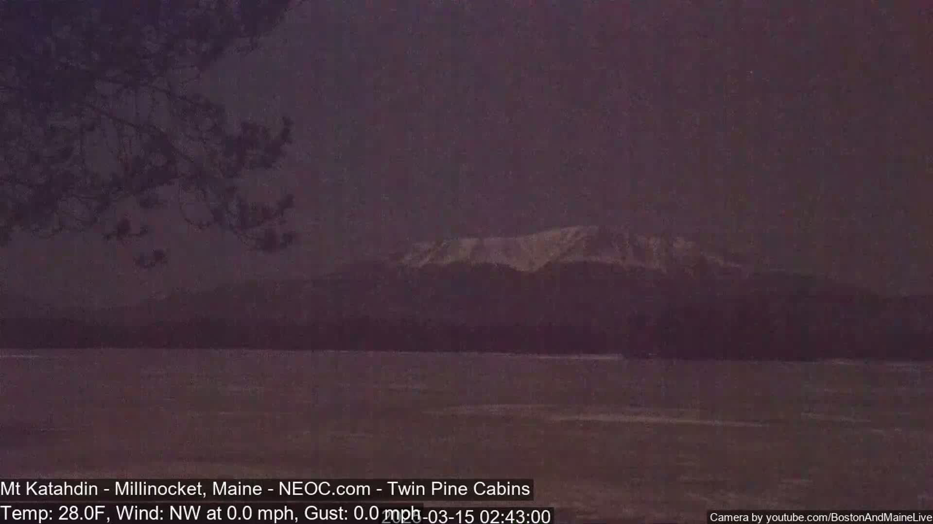 A snow-capped mountain is visible in the distance across a dark, calm body of water under a dusky sky.