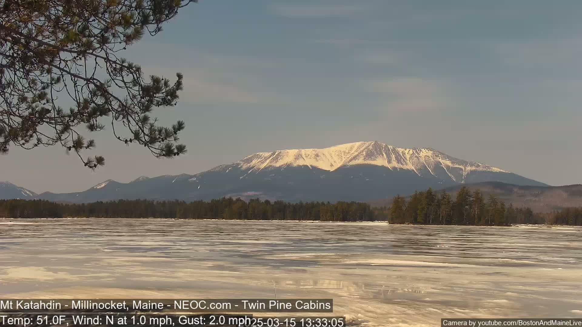 A partially frozen lake stretches before a snow-capped mountain range under a clear sky.