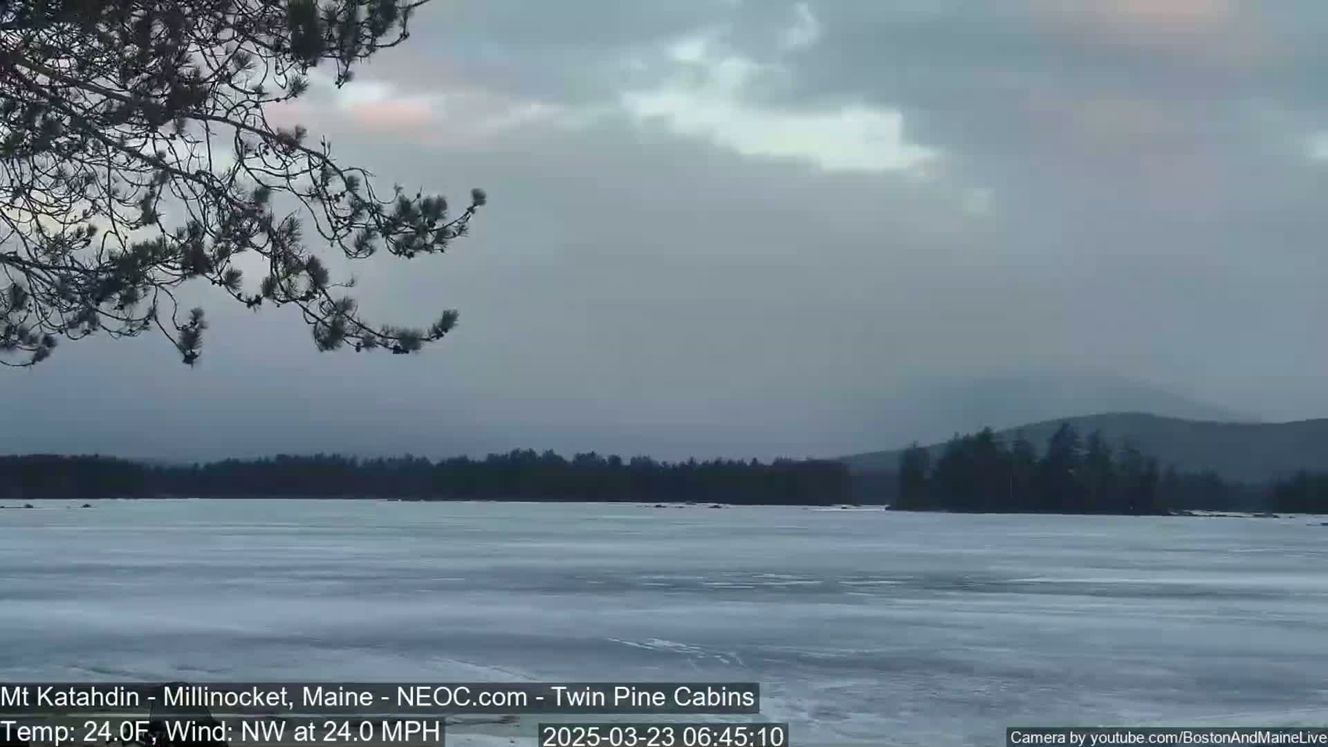 A frozen lake stretches to a distant, tree-covered shoreline under a cloudy, overcast sky.