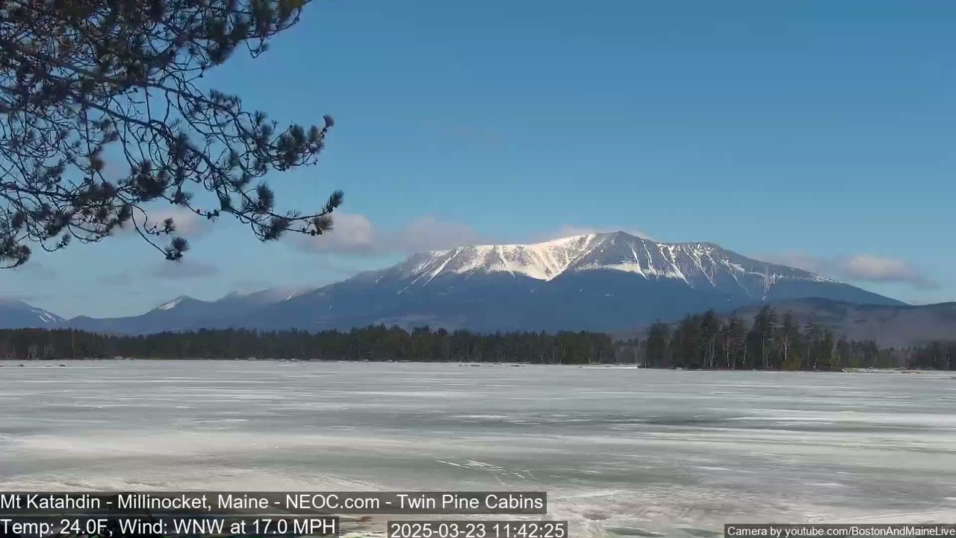 A snow-capped mountain range is visible across a frozen lake under a clear blue sky with a light wind.