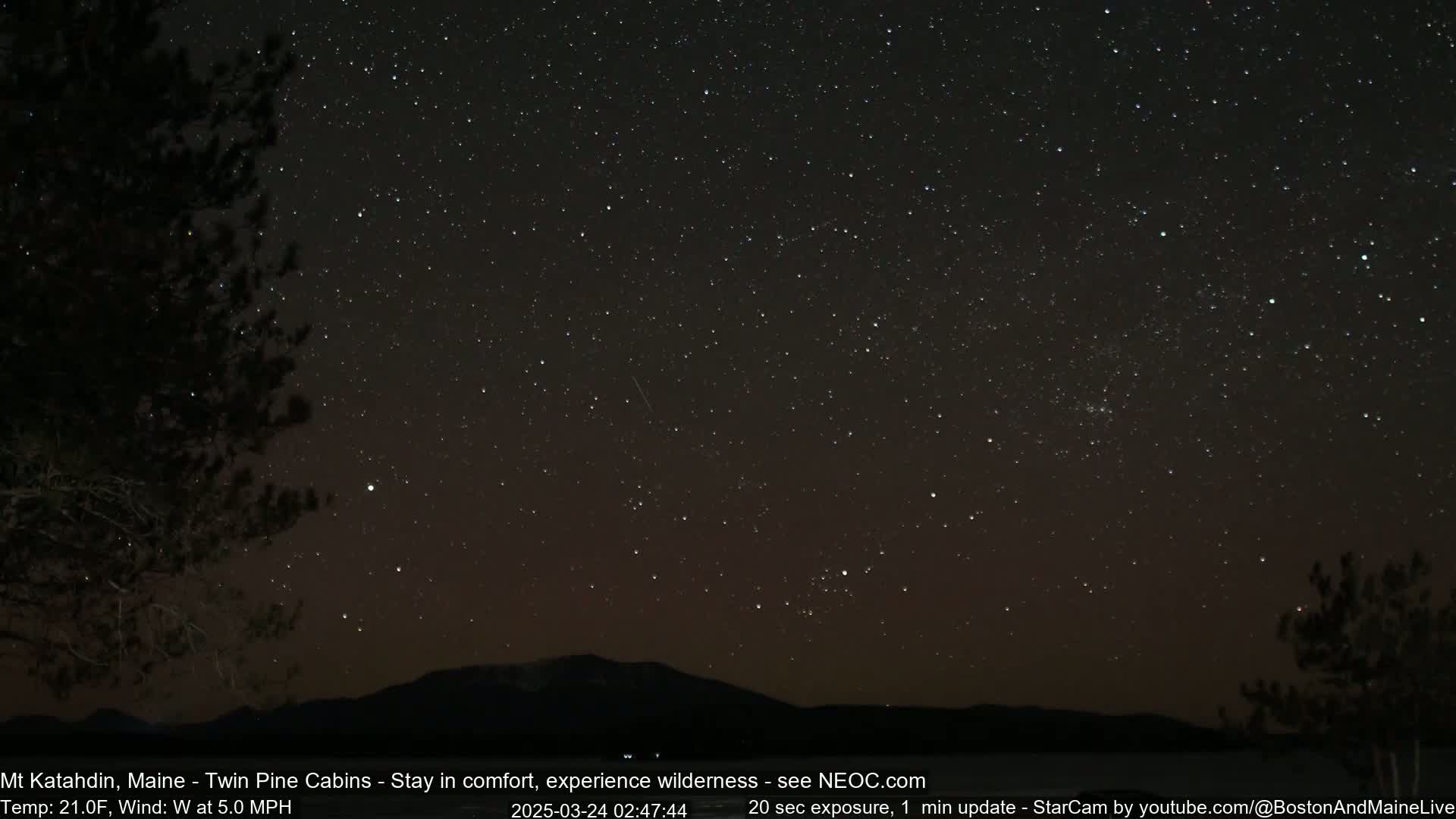 A nighttime landscape shows a dark silhouette of trees and a mountain range under a clear, star-filled sky with a shooting star visible.