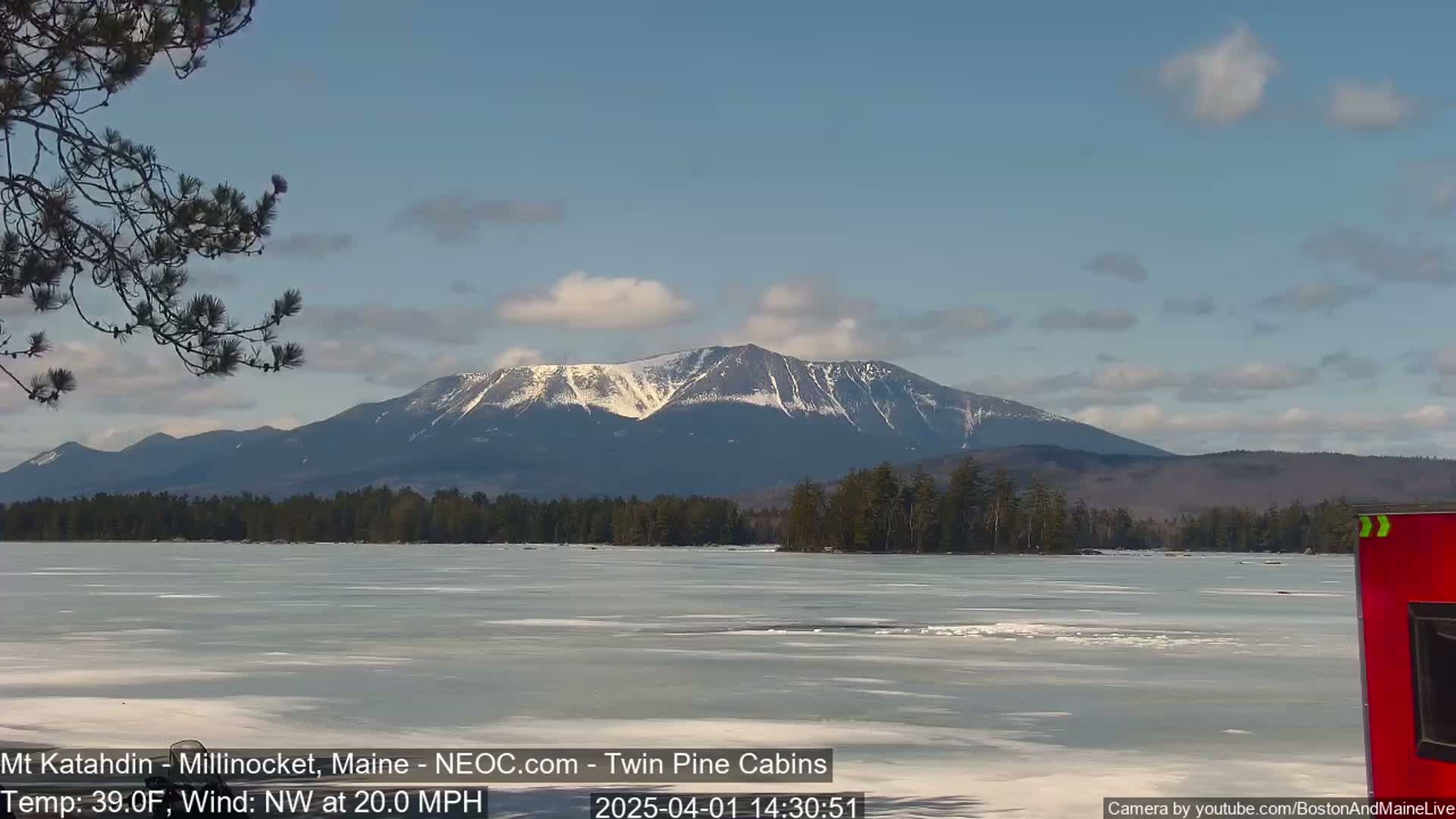A snow-capped mountain range is visible across a partially frozen lake under a partly cloudy sky.
