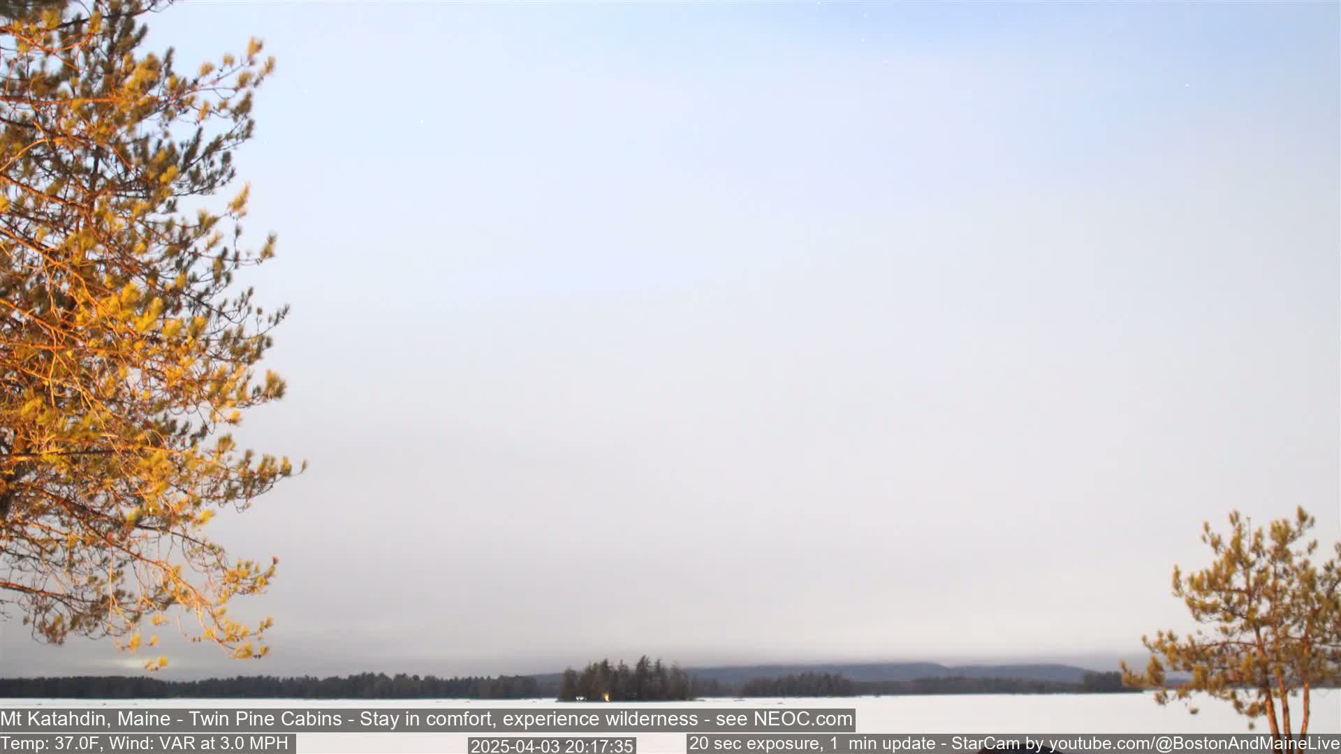 A hazy, pale sky over a snow-covered landscape with distant trees and a body of water under a pale sky.