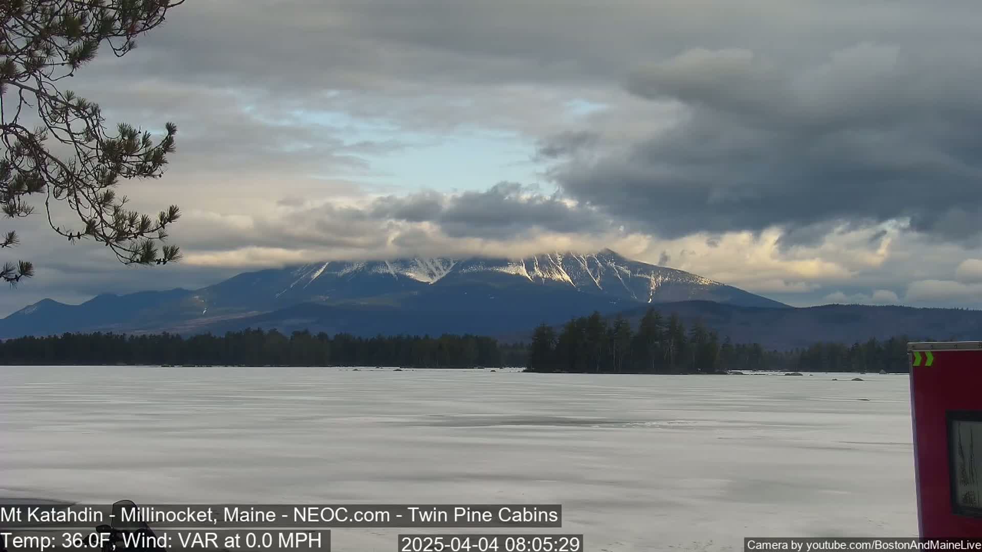 A snow-capped mountain range is visible in the distance across a frozen lake under a cloudy sky.