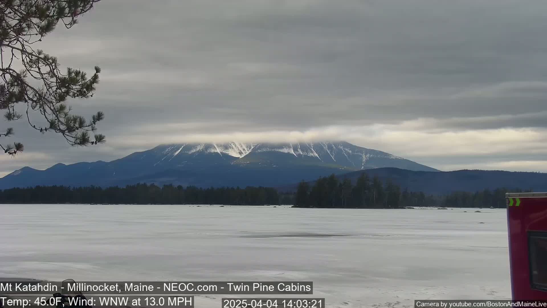 A snow-capped mountain range is visible in the distance across a frozen lake under a cloudy sky.
