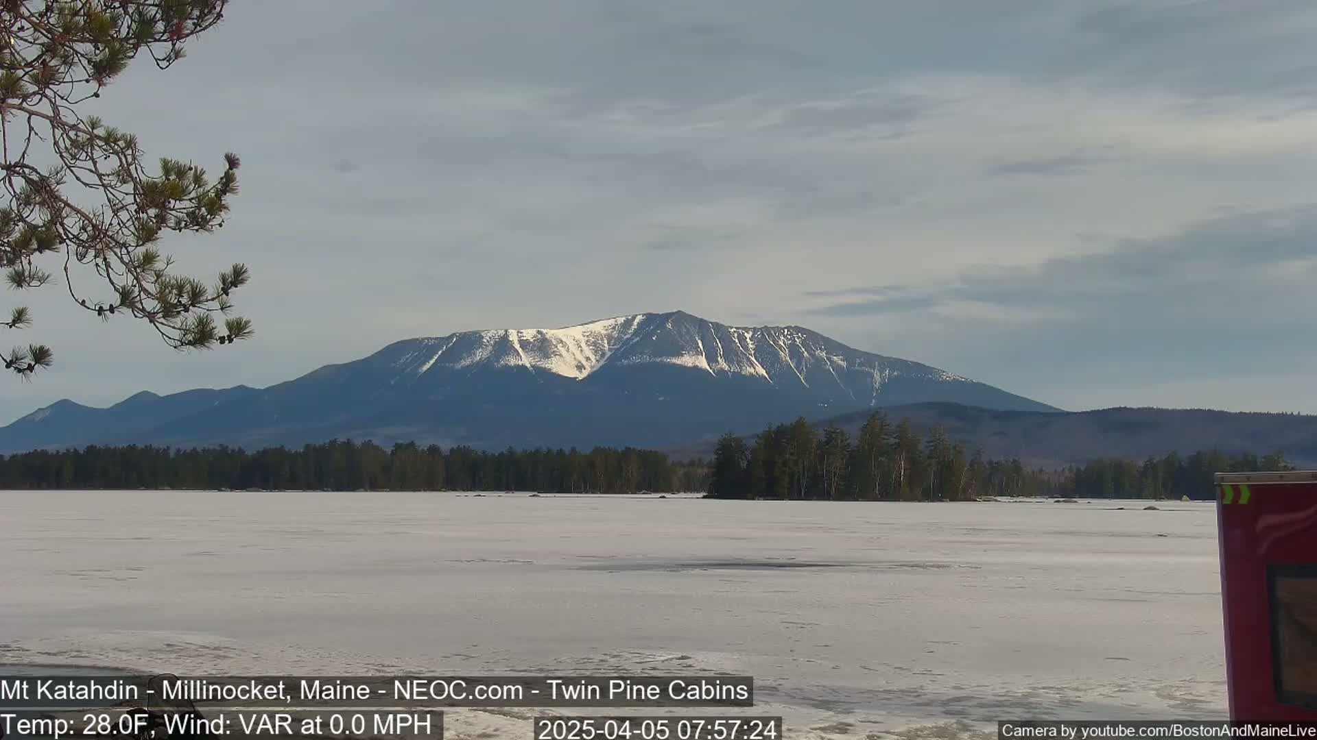 A snow-capped mountain is visible in the distance across a frozen lake under a partly cloudy sky.
