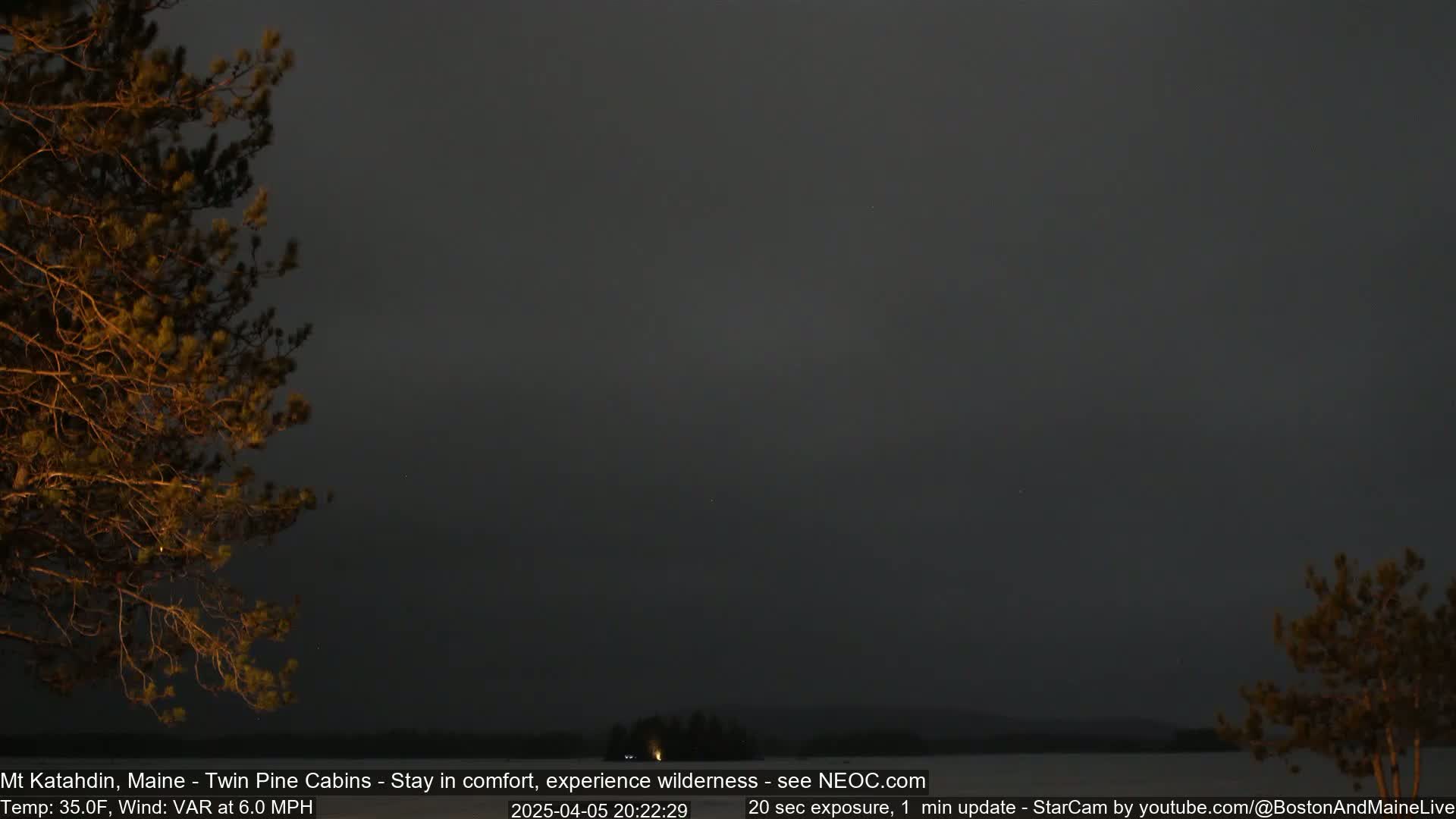 A nighttime, slightly hazy view of a lake, silhouetted trees, and a dark sky with a 6.0 mph wind and a temperature of 35 degrees Fahrenheit.