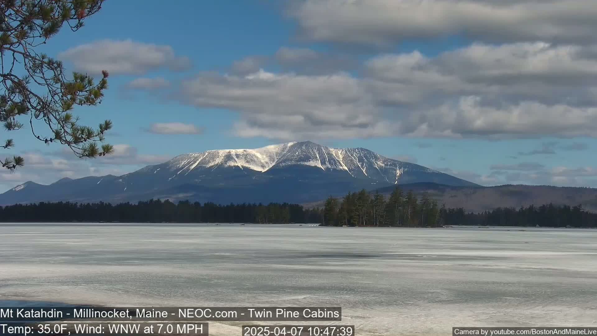 A snow-capped mountain range is visible in the distance across a partially frozen lake under a partly cloudy sky.