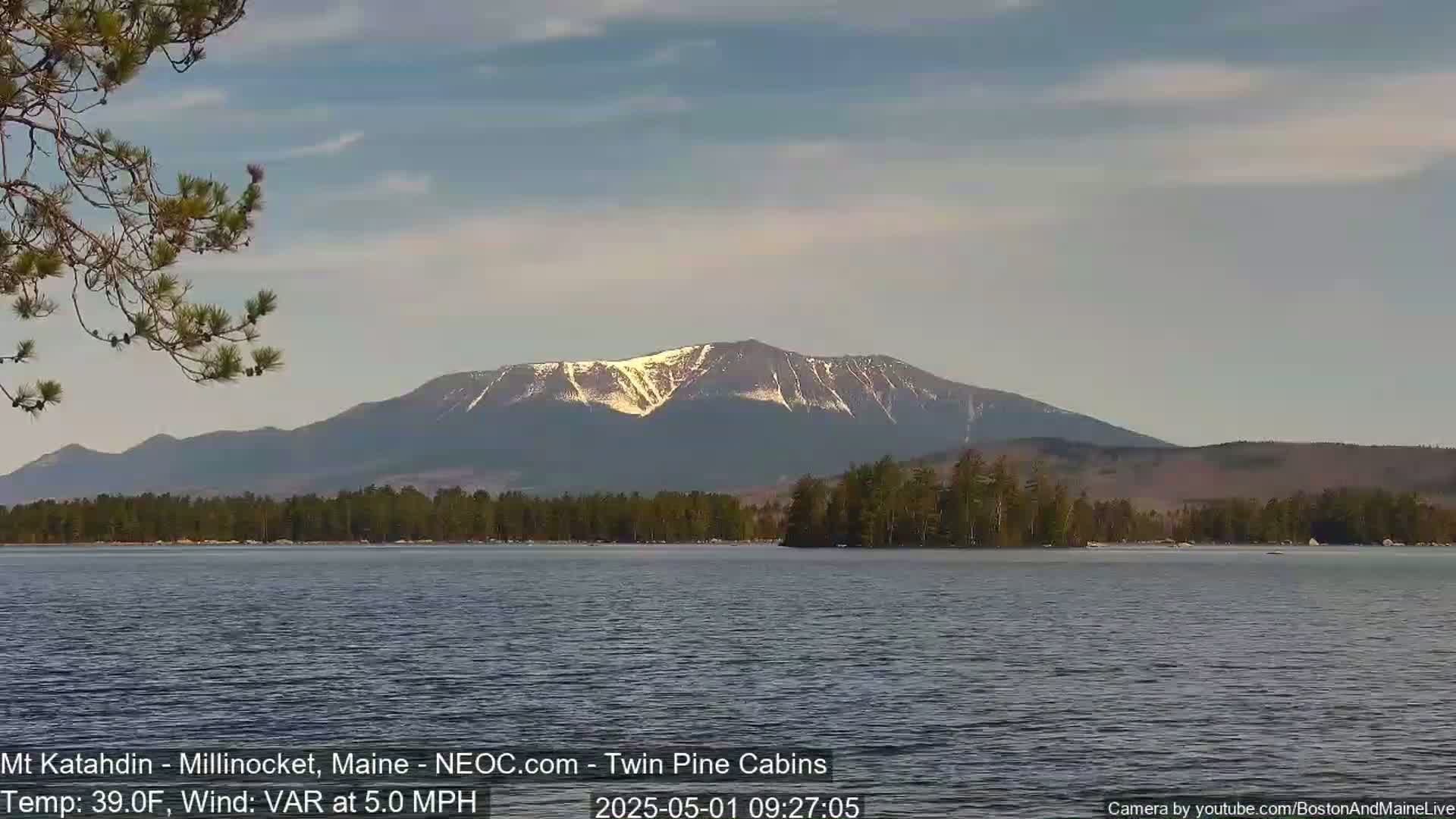 A calm lake with a snow-capped mountain in the background under a mostly clear sky.