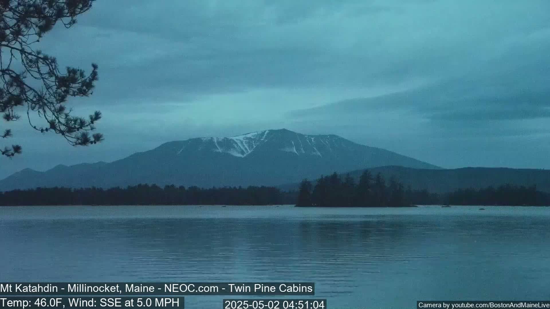 A calm lake reflects a snow-capped mountain range under a dusky blue sky.