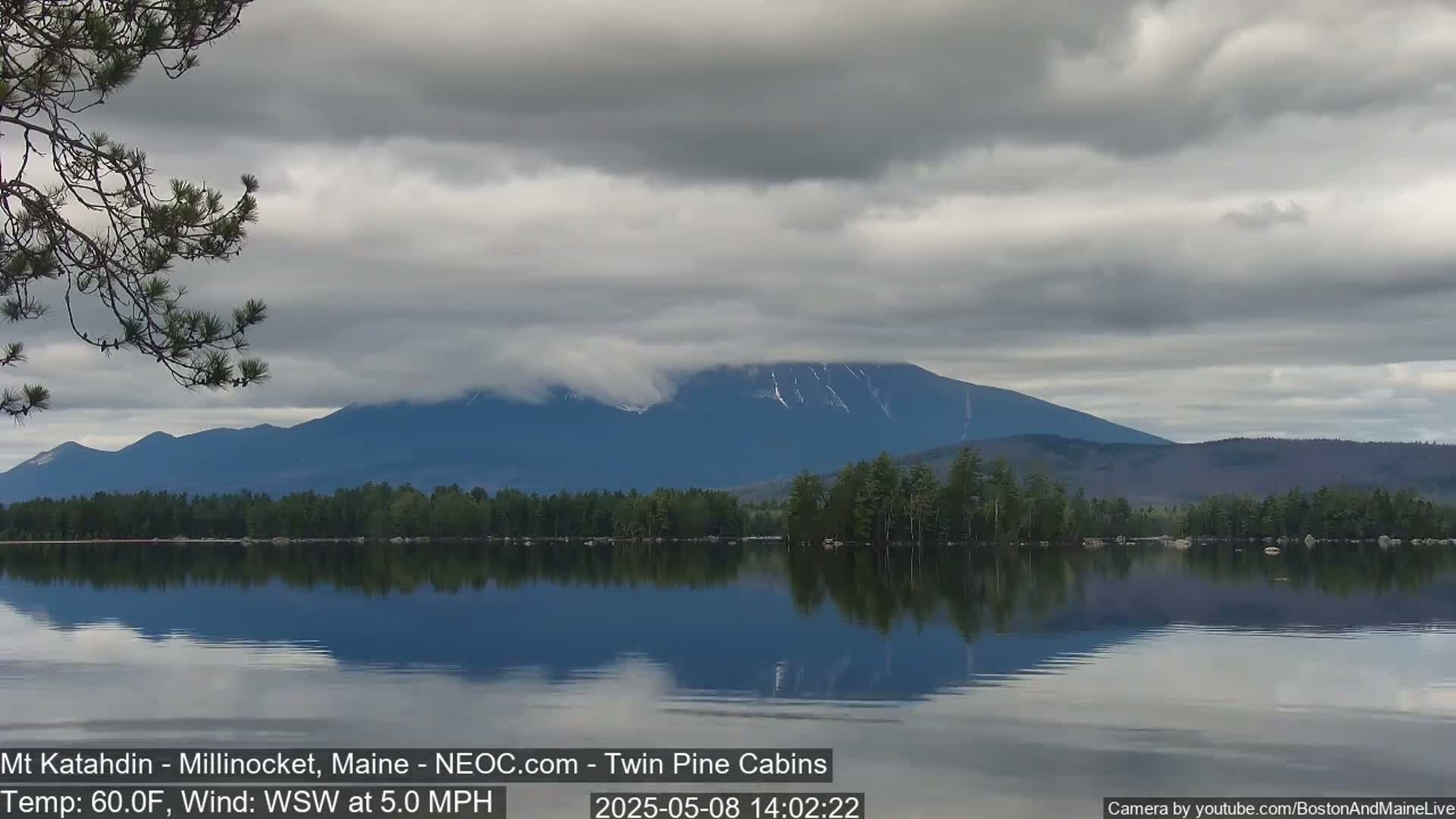 A calm lake reflects a mountain range under a cloudy sky.