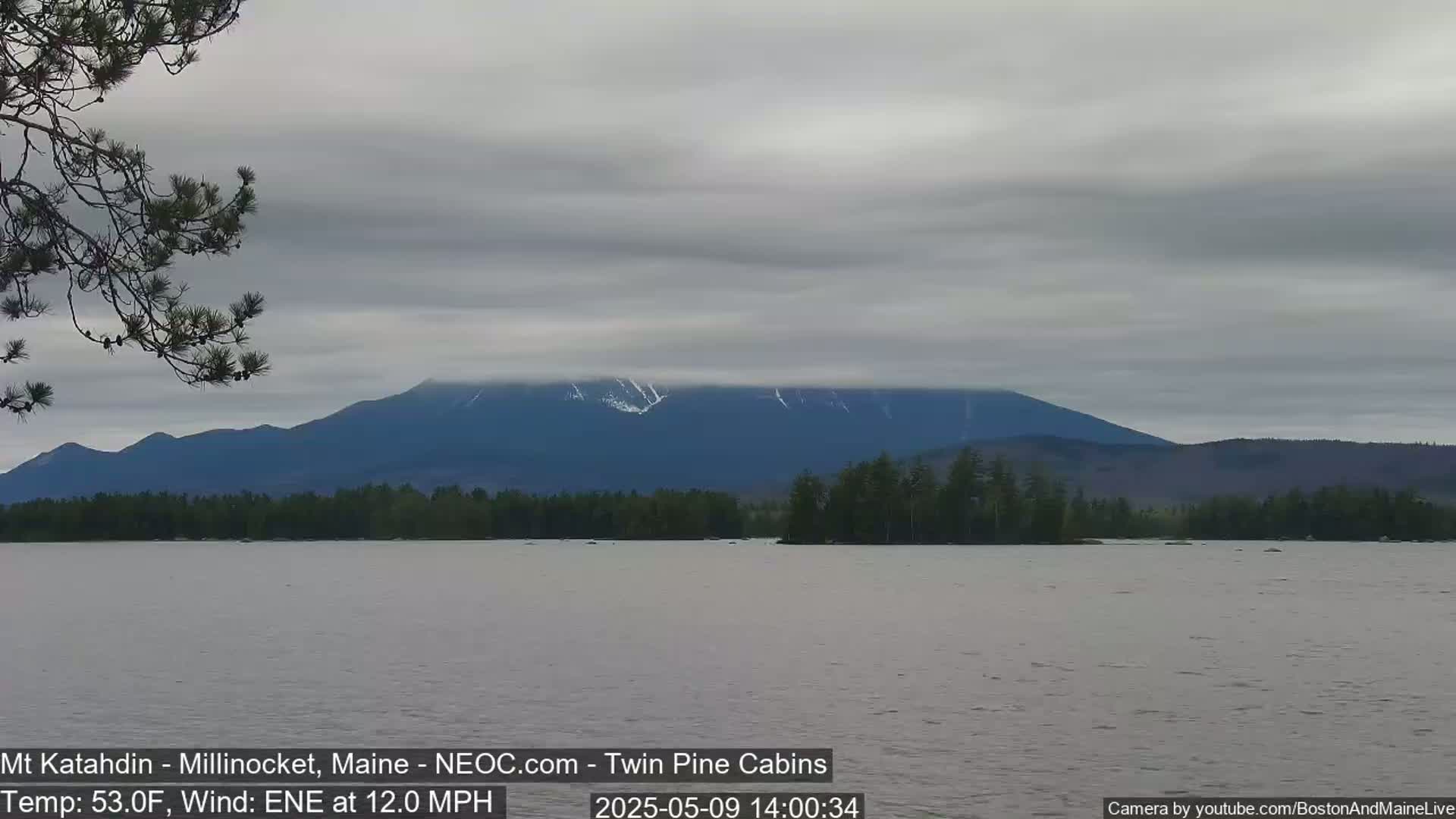 A calm lake with a mountain range in the background under a cloudy sky.