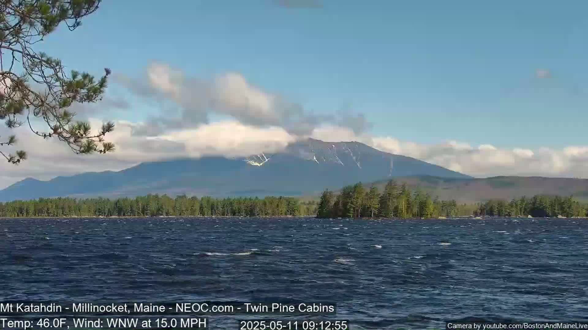 A partly cloudy day shows a partly snow-capped mountain range across a choppy lake with a WNW wind at 15 mph and a temperature of 46°F.