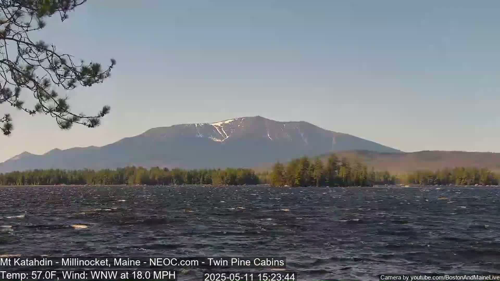 A windy lake with choppy waves stretches to a distant mountain range, partially covered in snow, under a clear sky.