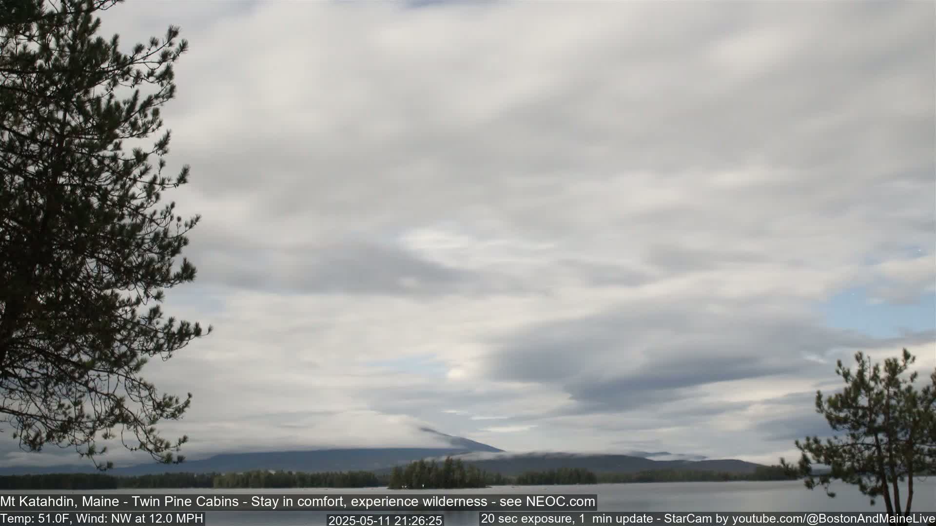 A mostly cloudy sky hangs over a calm lake and distant mountains partially shrouded in fog under a northwesterly wind.