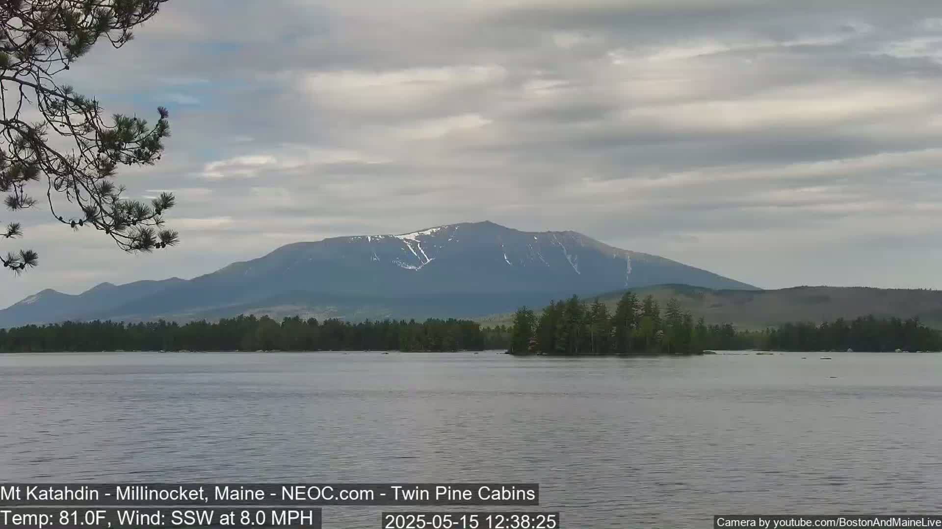 A calm lake with a mountain range in the background under a partly cloudy sky.
