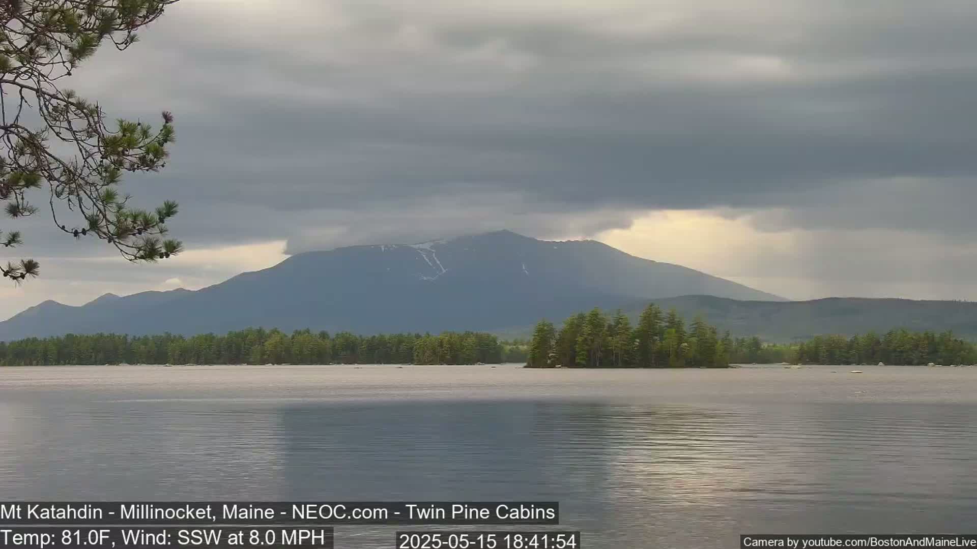 A calm lake reflects a mountain range under a mostly cloudy sky.