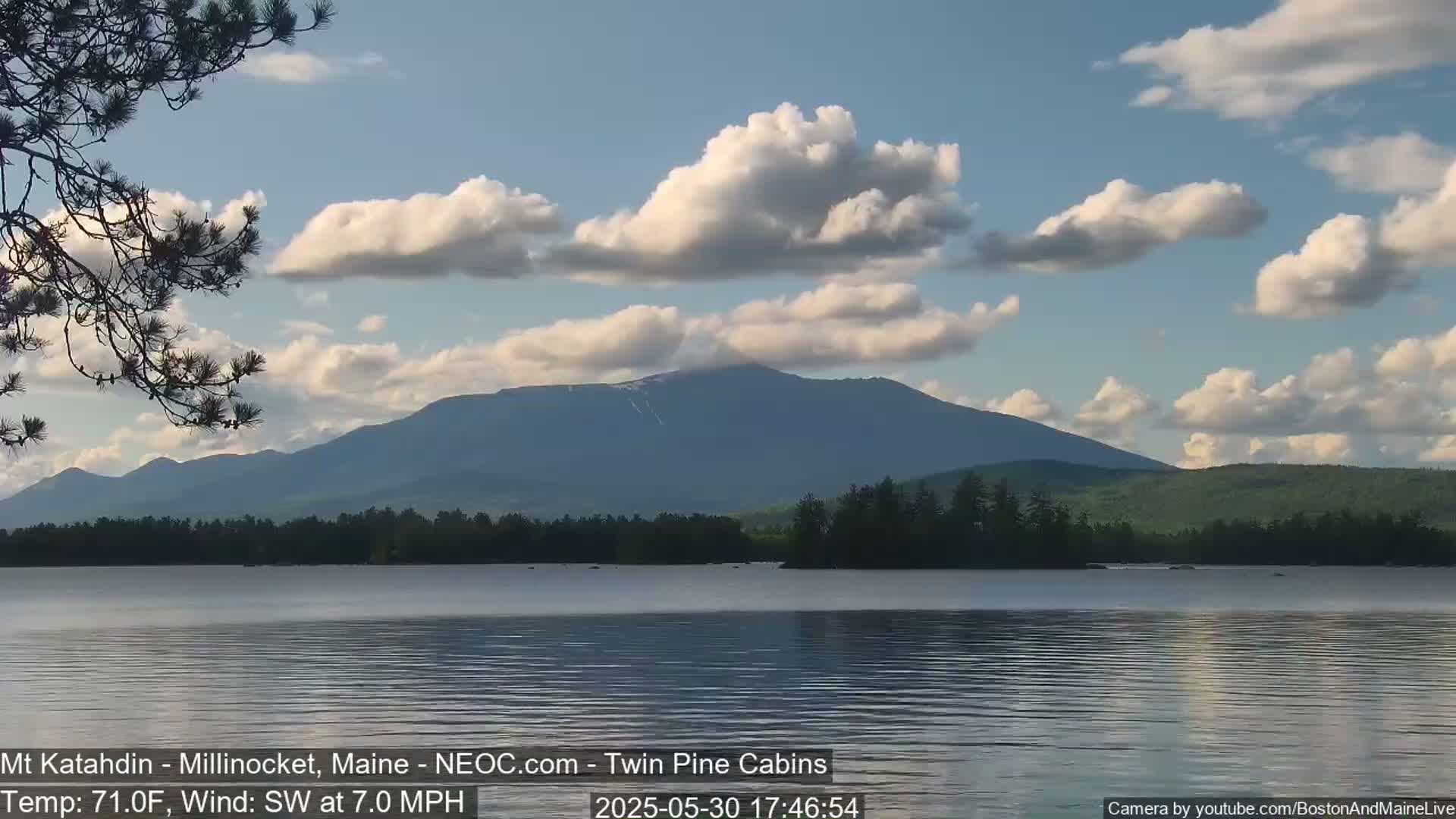 A calm lake reflects a mountain range under a partly cloudy sky.