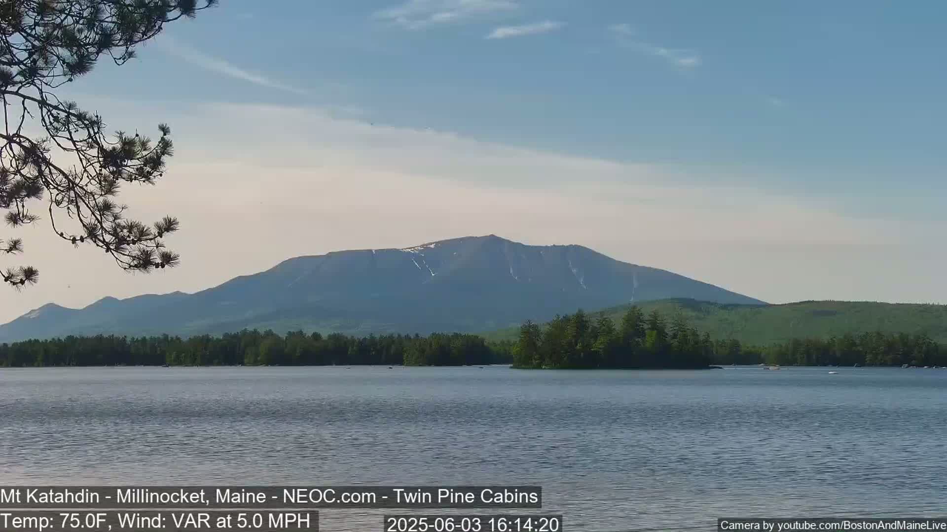 A calm lake with a mountain range in the background under a clear, partly cloudy sky.