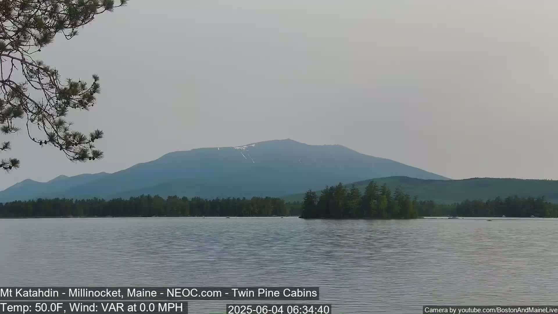 A calm lake reflects a hazy mountain range under a muted sky.