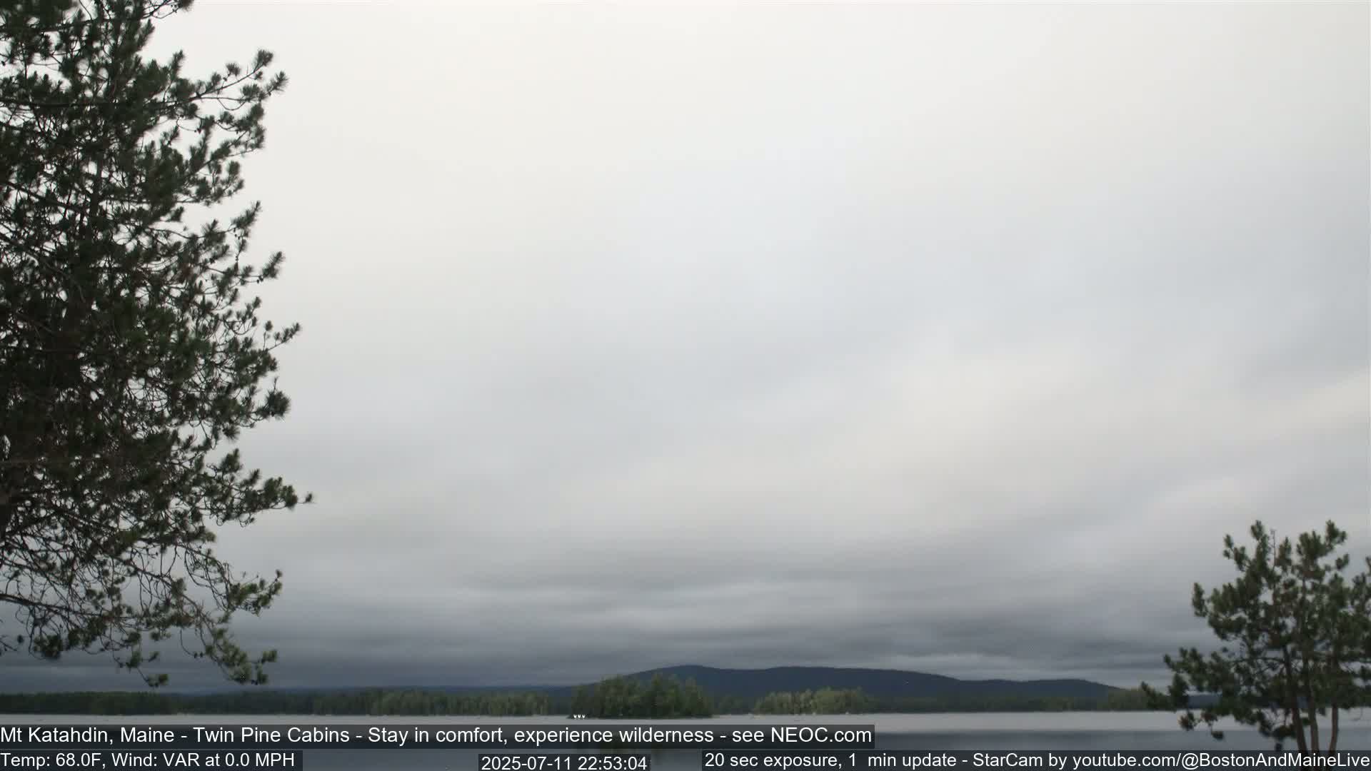 A mostly cloudy sky overlooks a calm body of water and distant trees under a pale gray sky.