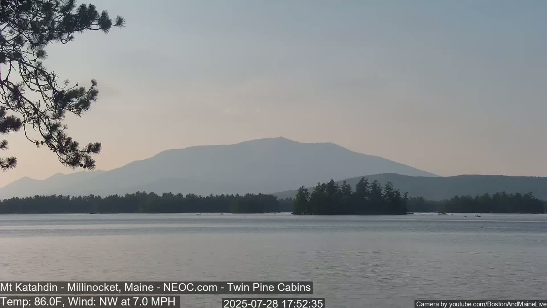 A calm lake with a distant mountain range under a hazy sky.