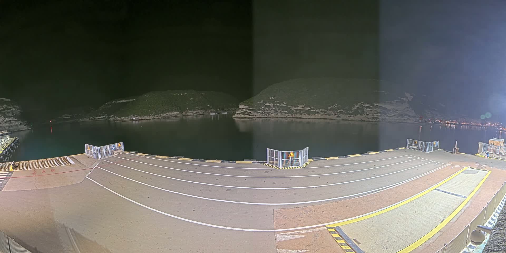 A nighttime view of an empty ferry dock with calm water and hills in the background.