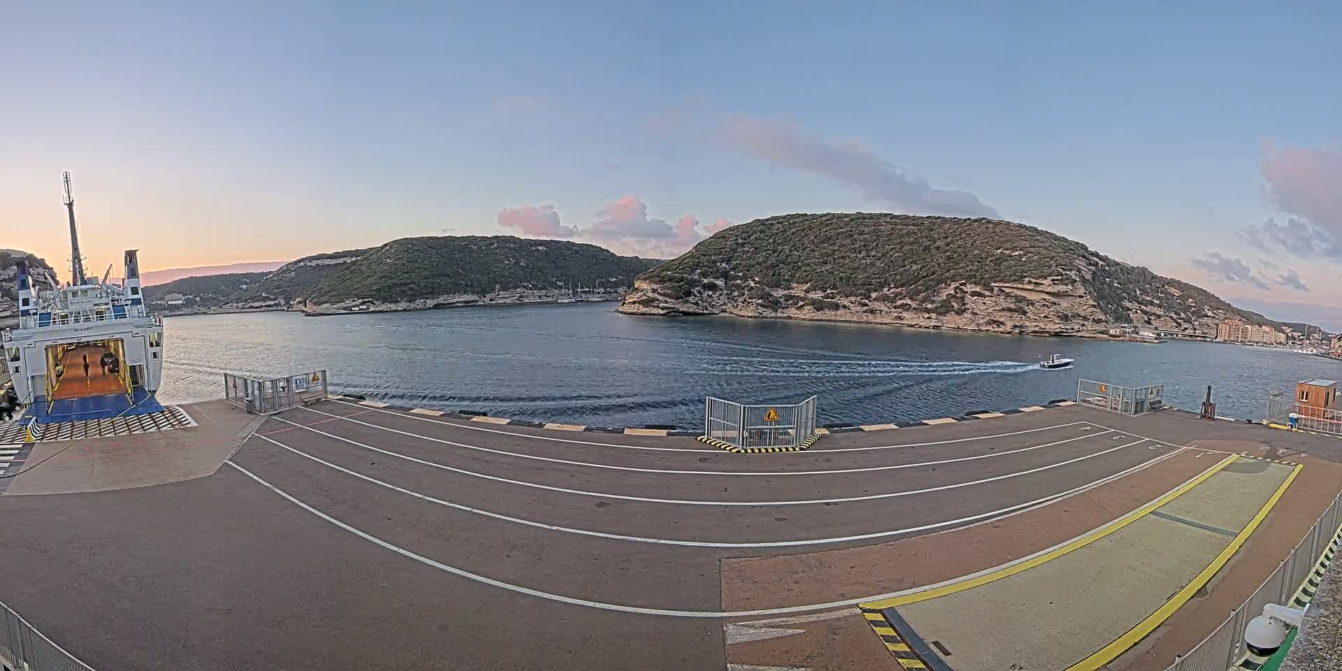 A ferry is docked at a port, with calm water and a partly cloudy sky at dusk.