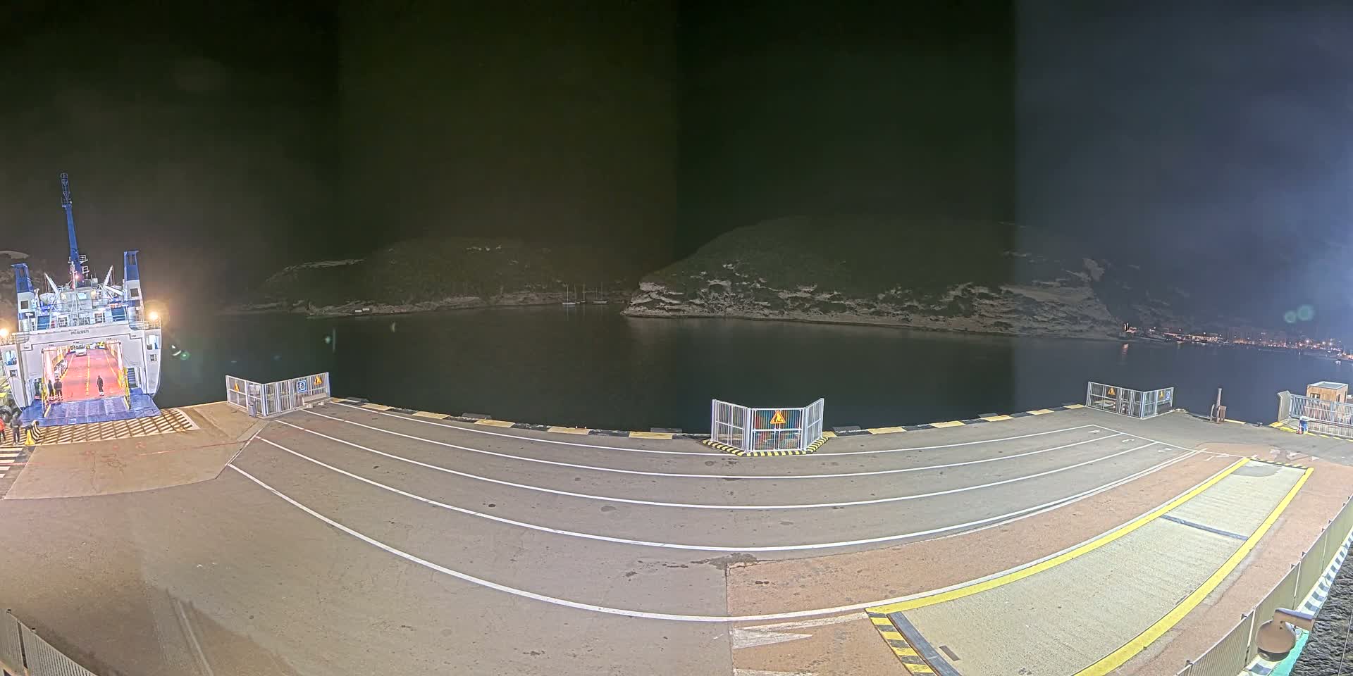 A ferry is docked at a port at night, with calm water surrounding a small, rocky cove.