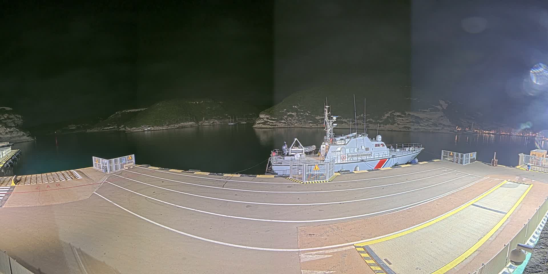 A large vessel is docked at a nighttime port, under a dark, cloudy sky.