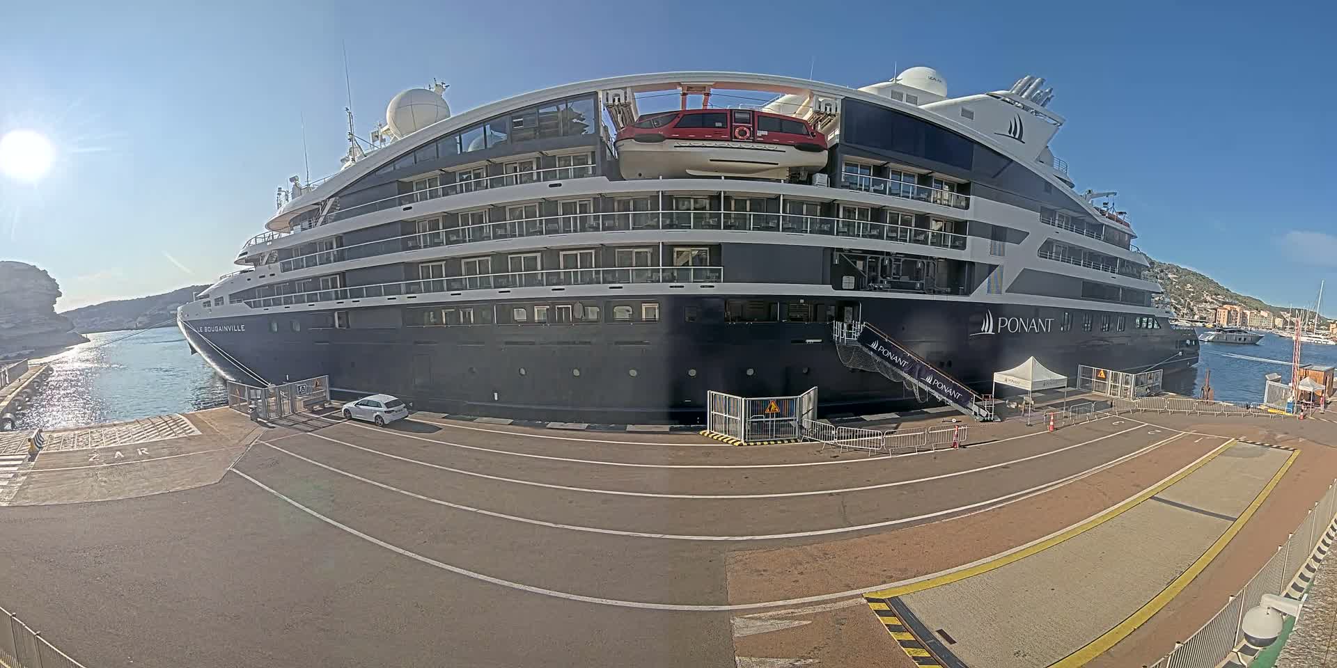 A large, dark-colored cruise ship is docked at a port on a sunny day.