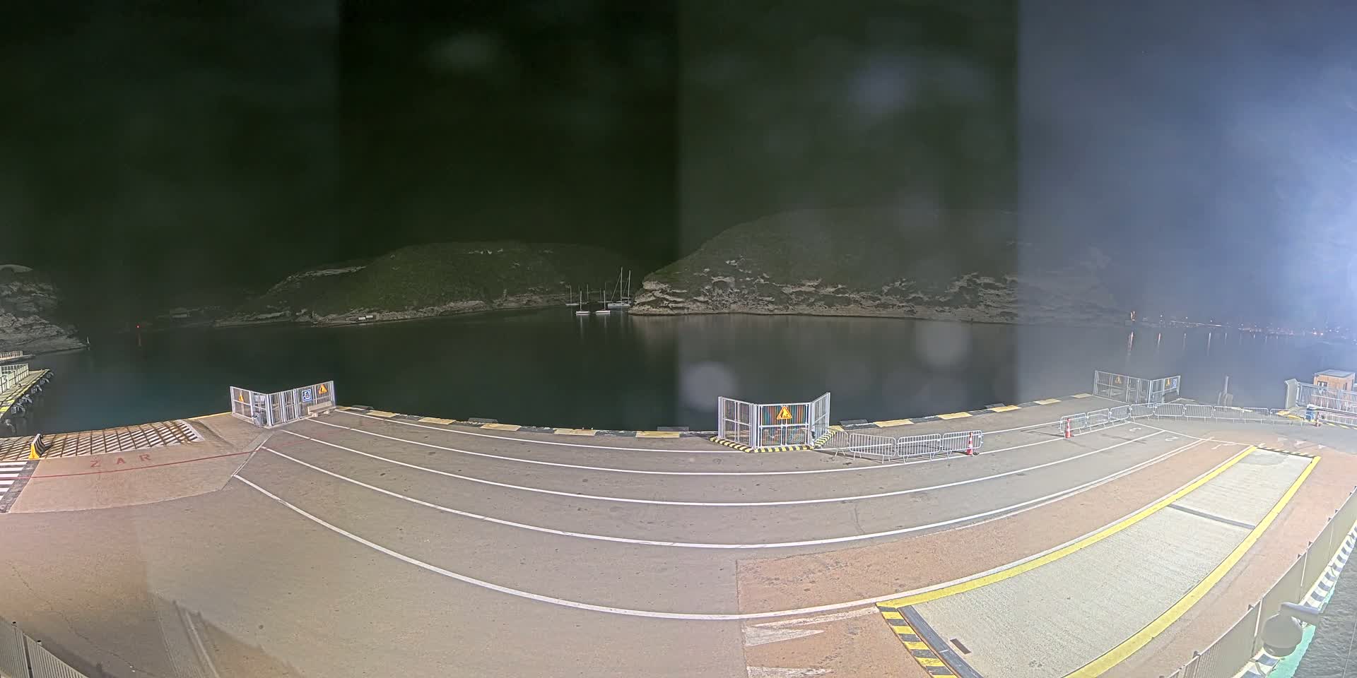 A nighttime view of an empty ferry terminal overlooking a calm body of water surrounded by dark hills.