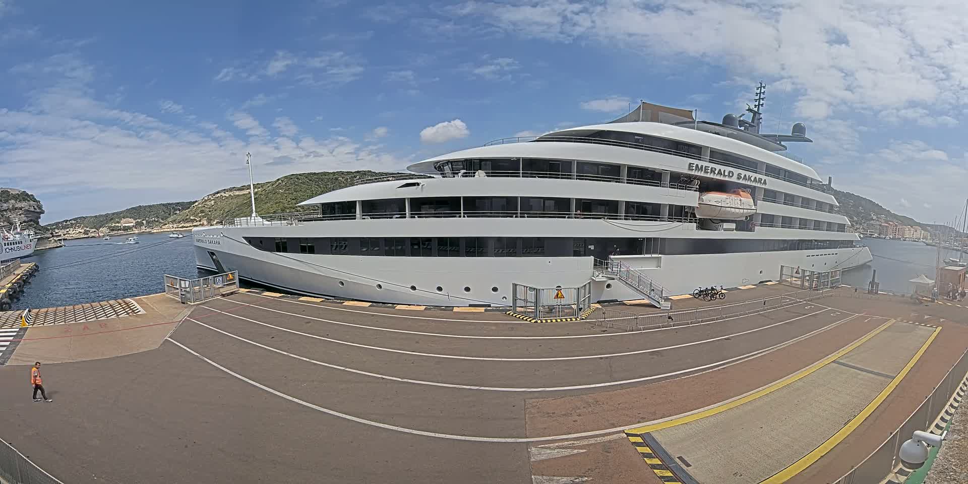A large white yacht is docked at a port on a partly cloudy day.