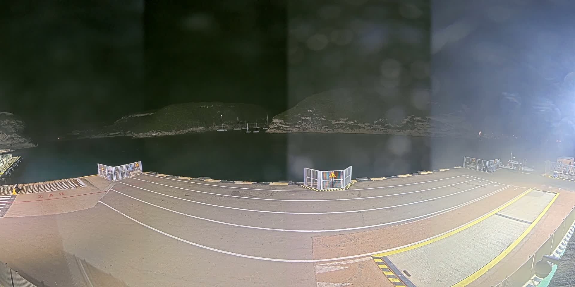 A nighttime view of an empty ferry dock with a calm body of water and hills in the background.