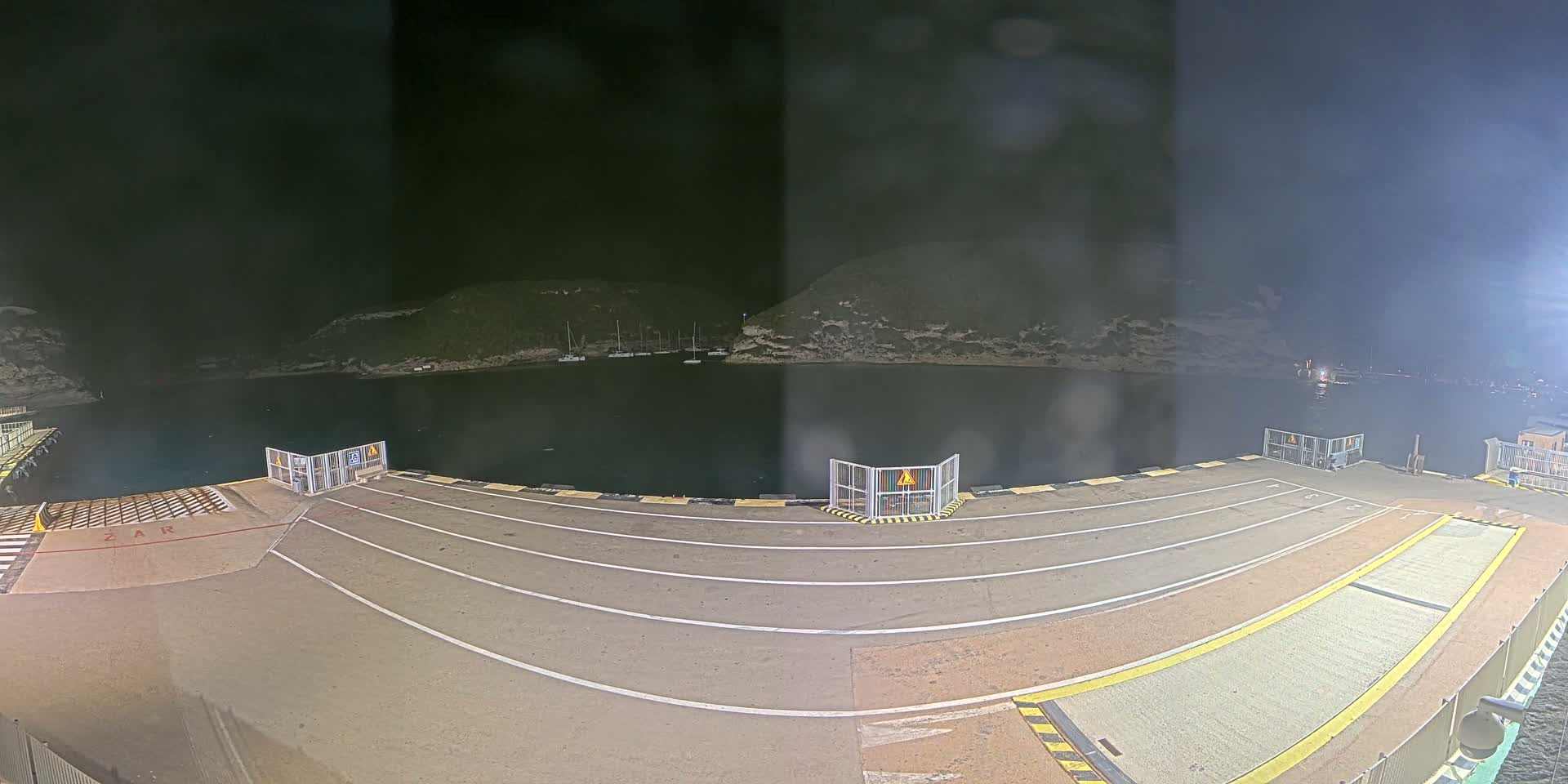 An empty ferry dock at night, overlooking a dark body of water with hills in the background under a dark sky.