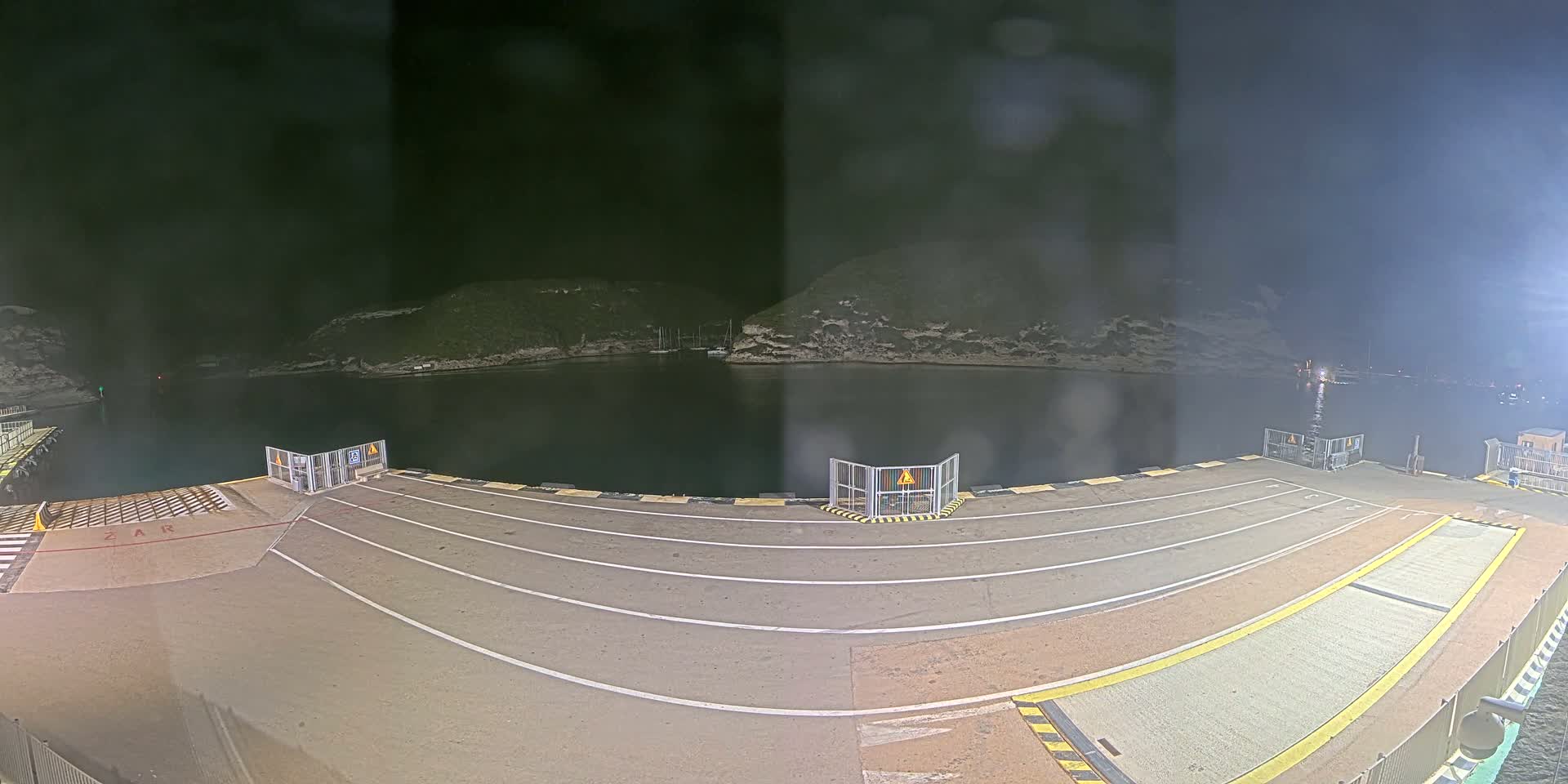 A nighttime view of a ferry terminal with a calm body of water and hills in the background.